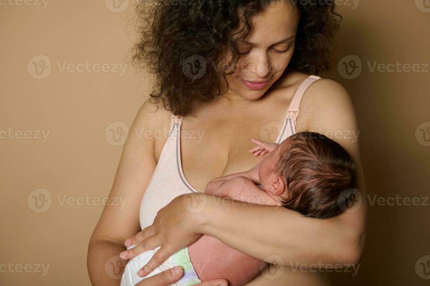 Close-up happy woman, loving caring happy mother smiles looking at her newborn baby, she holds in arms, beige background photo