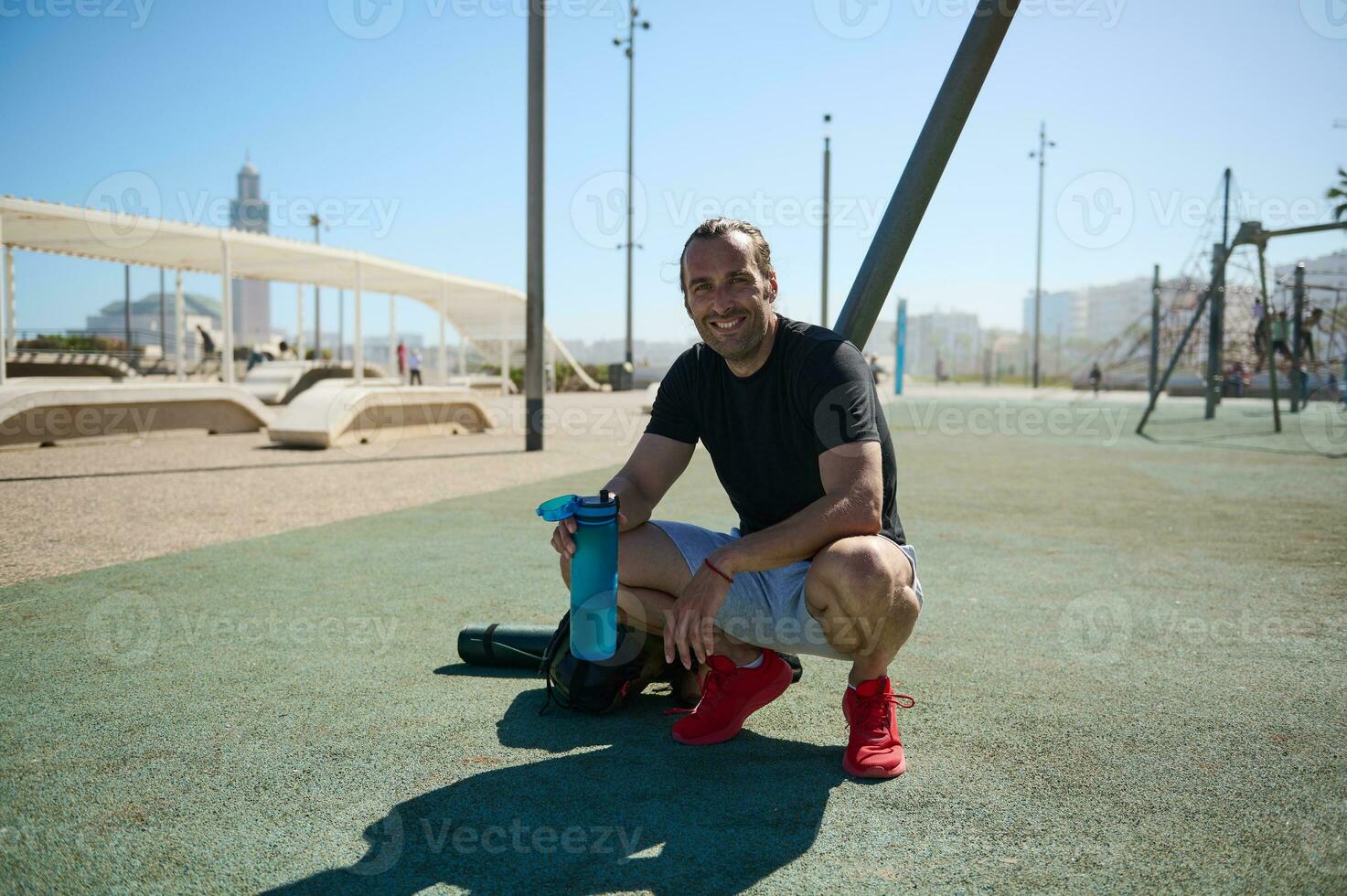 Handsome Caucasian male athlete looking at camera while relaxing after heavy workout in the outdoor urban sportsground photo