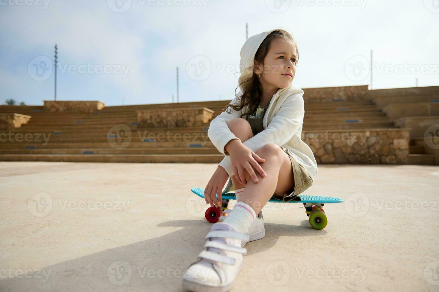 adorable pequeño niña mirando lejos, sentado en su patineta, soñando mirando lejos. gente. infancia. ocio actividad foto