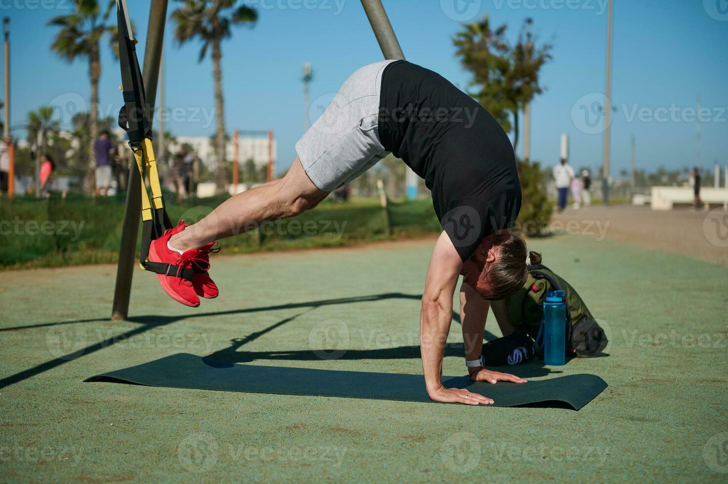 Young athletic man in sports clothing training legs with suspension fitness straps in an outdoor sports ground photo