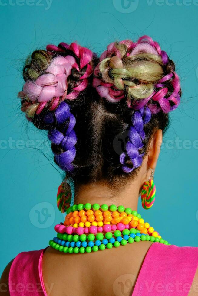 encantador niña con un multicolor trenzas peinado y brillante constituir, posando en estudio en contra un azul antecedentes. foto