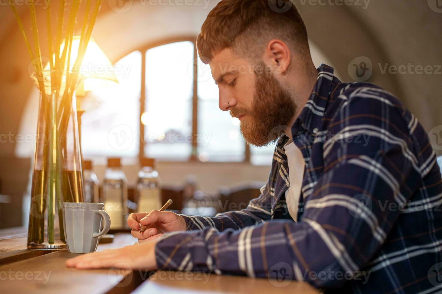 Young bearded businessman sits in cafe, home at table and writes in notebook. Man is working, studying. photo