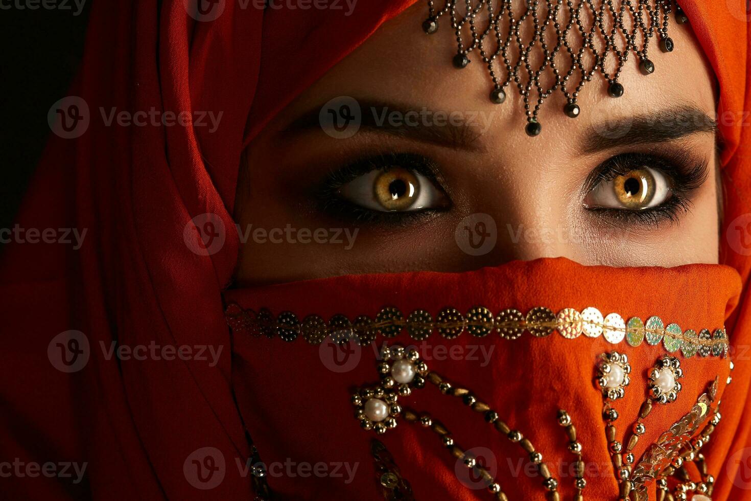 Studio shot of a young charming woman wearing the terracotta hijab decorated with sequins and jewelry. Arabic style. photo