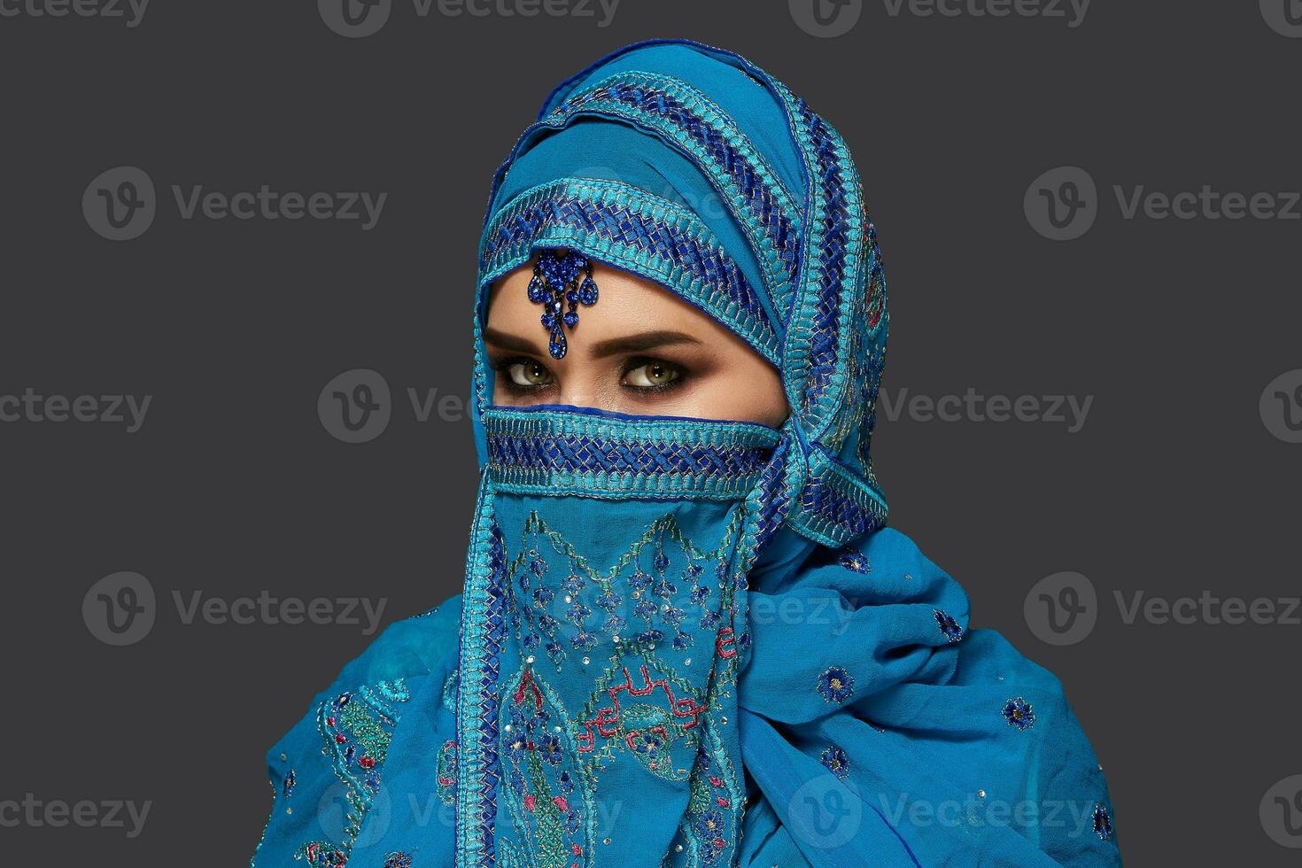 Studio shot of a young beautiful woman wearing the blue hijab decorated with sequins and jewelry. Arabic style. photo