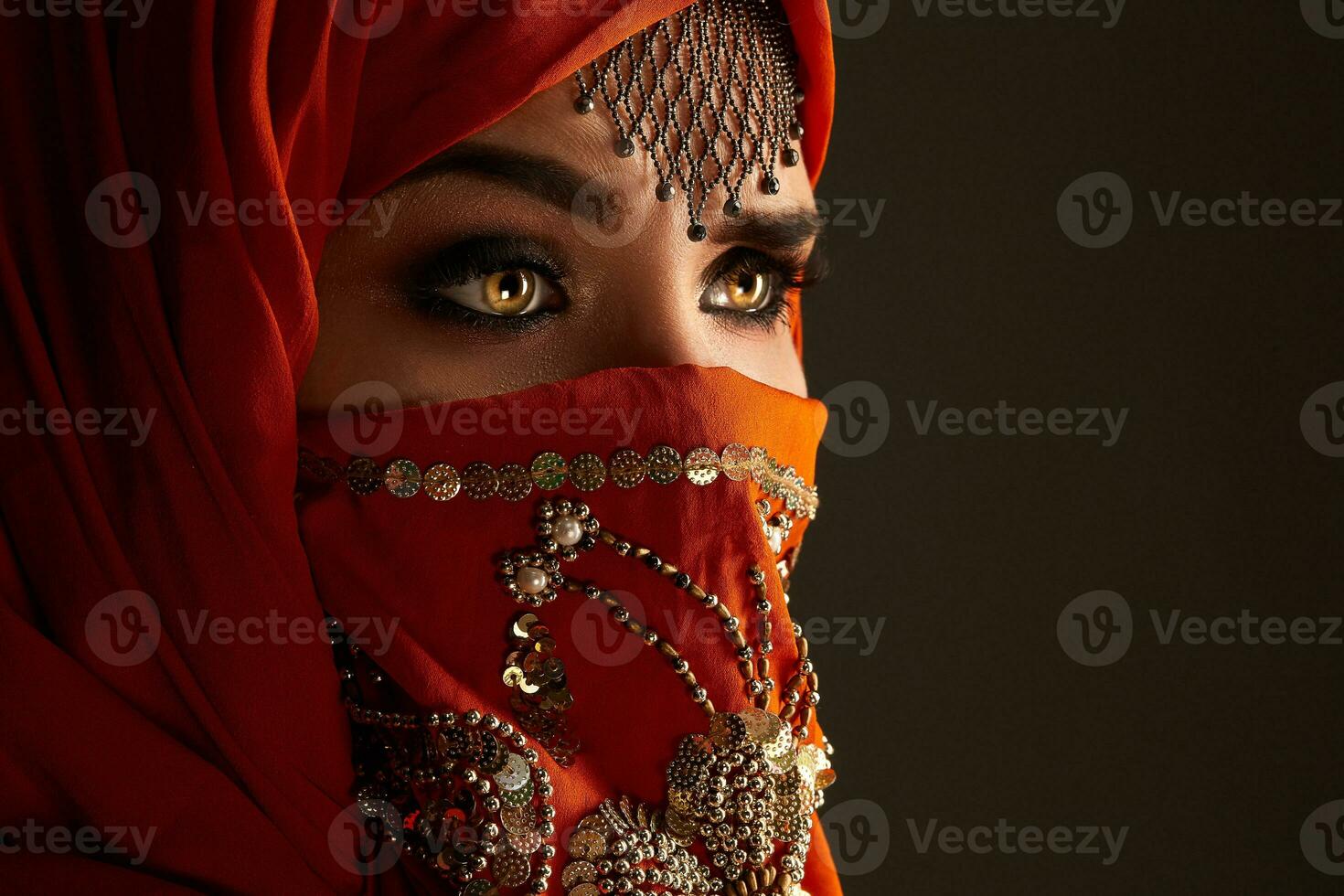 Studio shot of a young charming woman wearing the terracotta hijab decorated with sequins and jewelry. Arabic style. photo