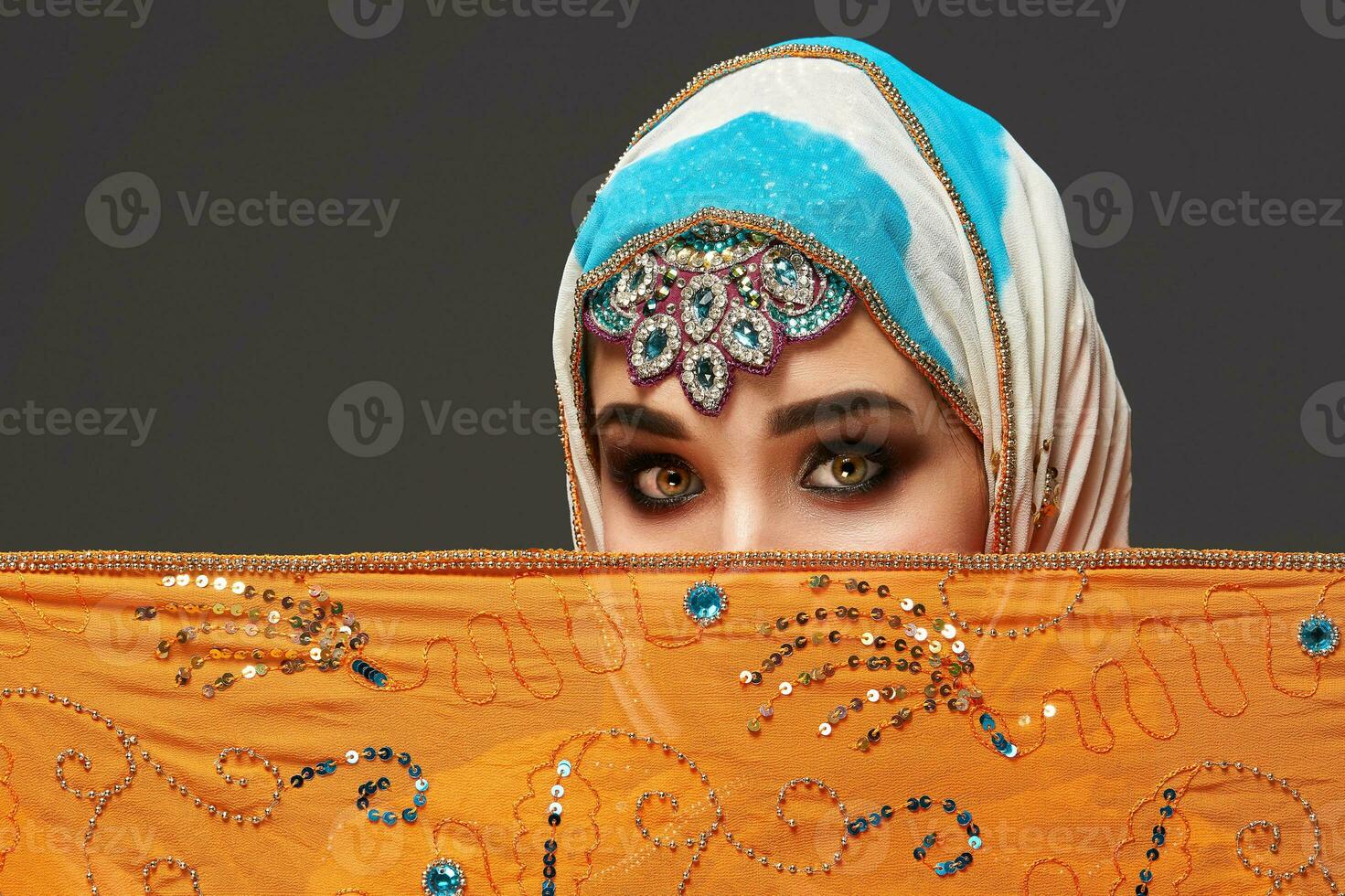 Studio shot of a chrming female wearing the colorful hijab decorated with sequins and jewelry. Arabic style. photo