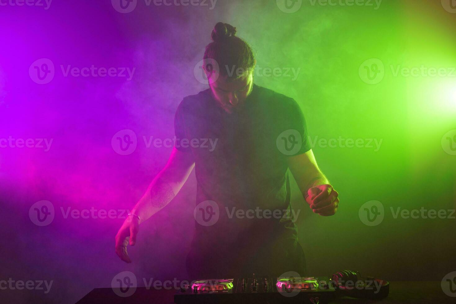 DJ at work mixing sound on her decks at a party or night club with colourful smoke light background photo