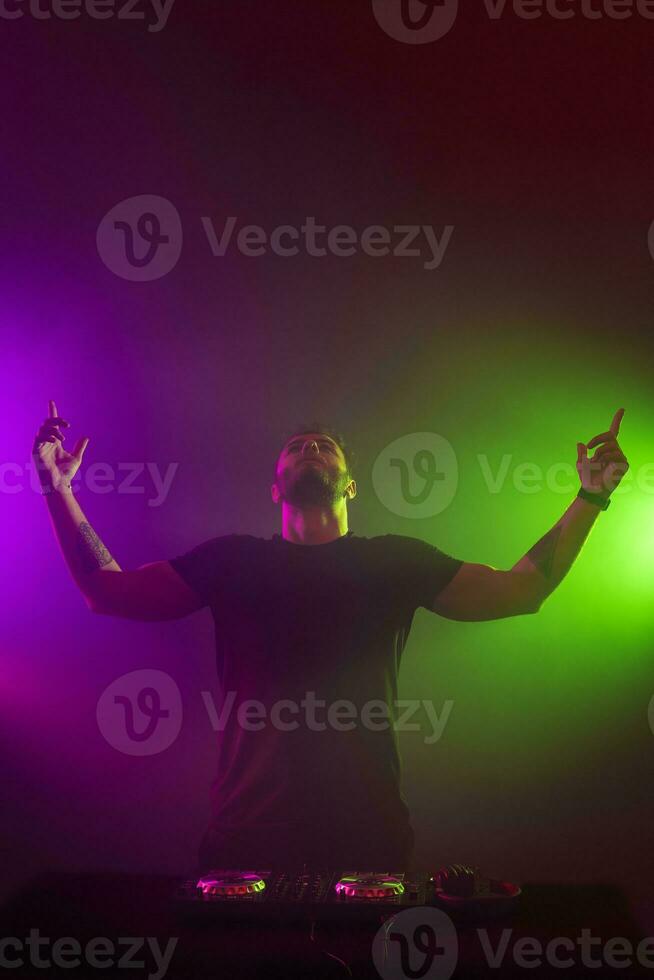 DJ at work mixing sound on her decks at a party or night club with colourful smoke light background photo