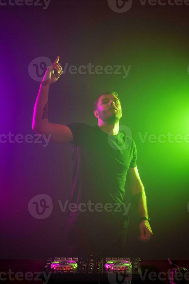 DJ at work mixing sound on her decks at a party or night club with colourful smoke light background photo