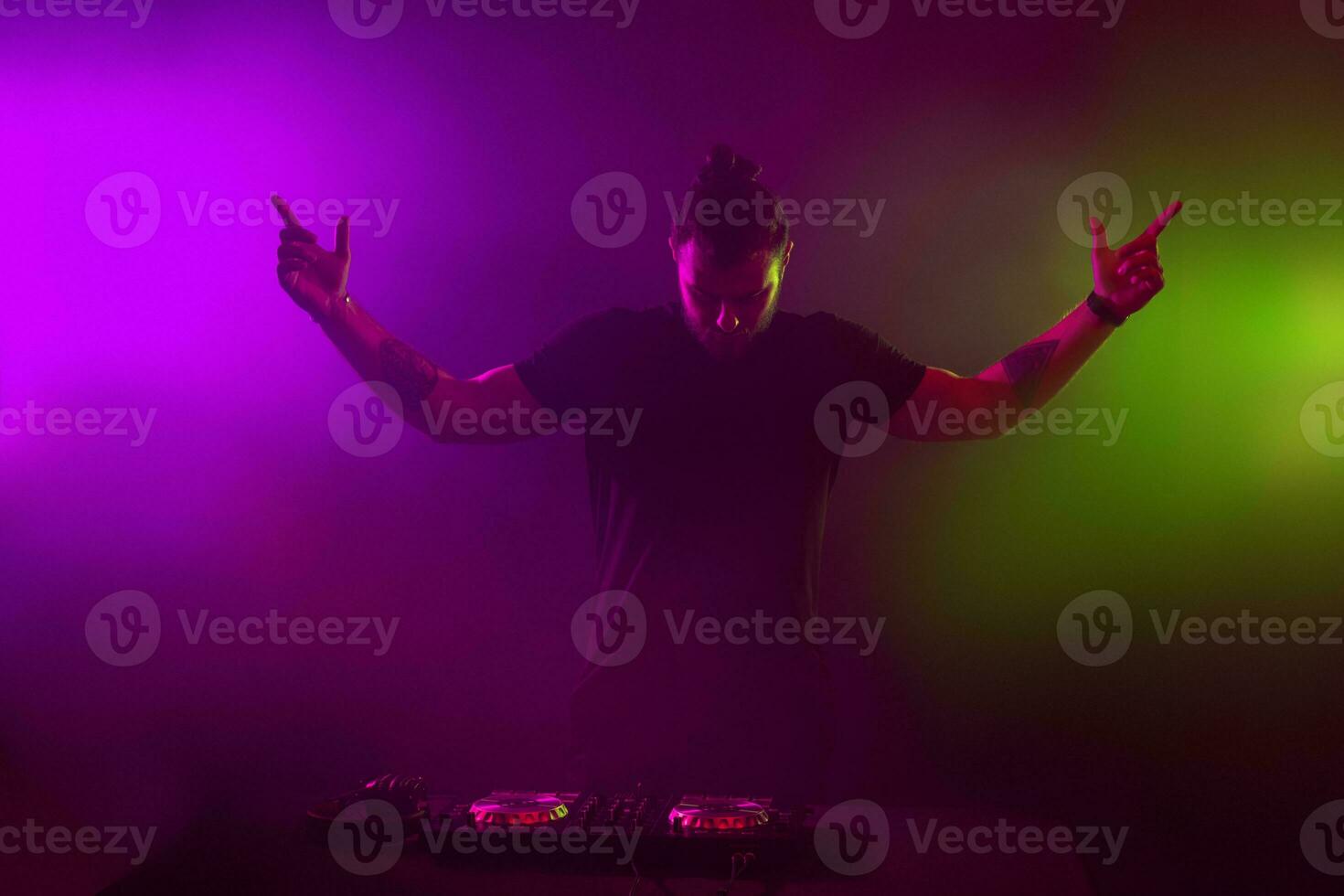 DJ at work mixing sound on her decks at a party or night club with colourful smoke light background photo