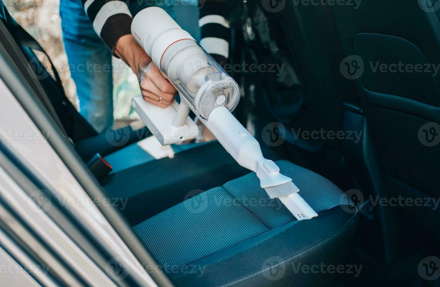 de cerca de un hombre Pasar la aspiradora un coche asiento. el mano sostiene un sin cable vacío limpiador y limpia el interior de el coche. foto