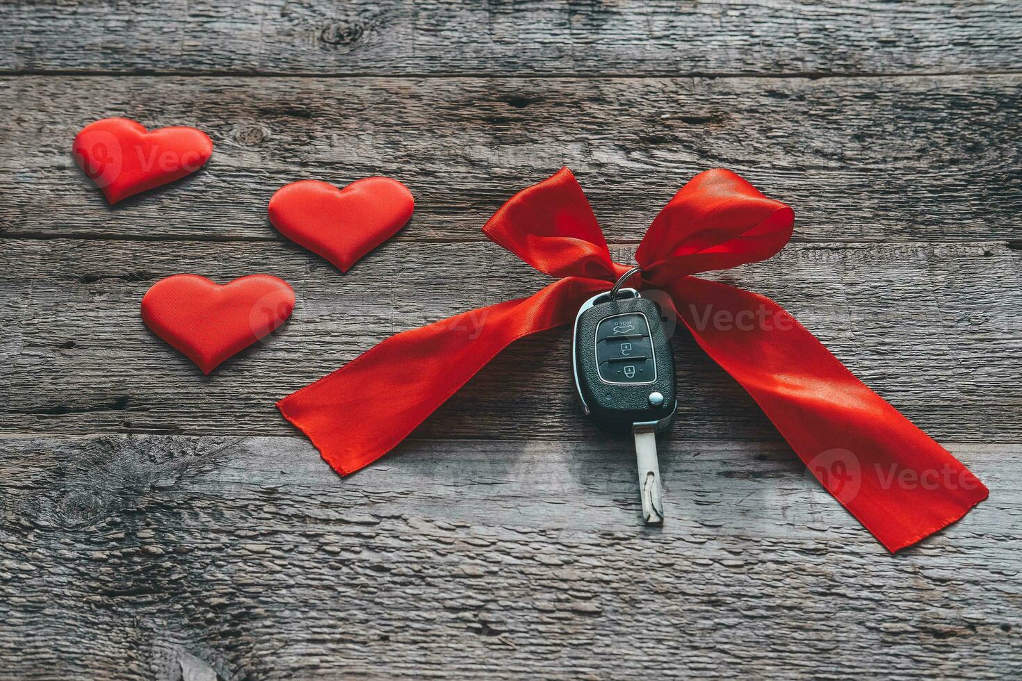 Car keys with red ribbon and heart on wooden background. The concept of a car gift for the holiday of February 14th. Valentine's Day. photo