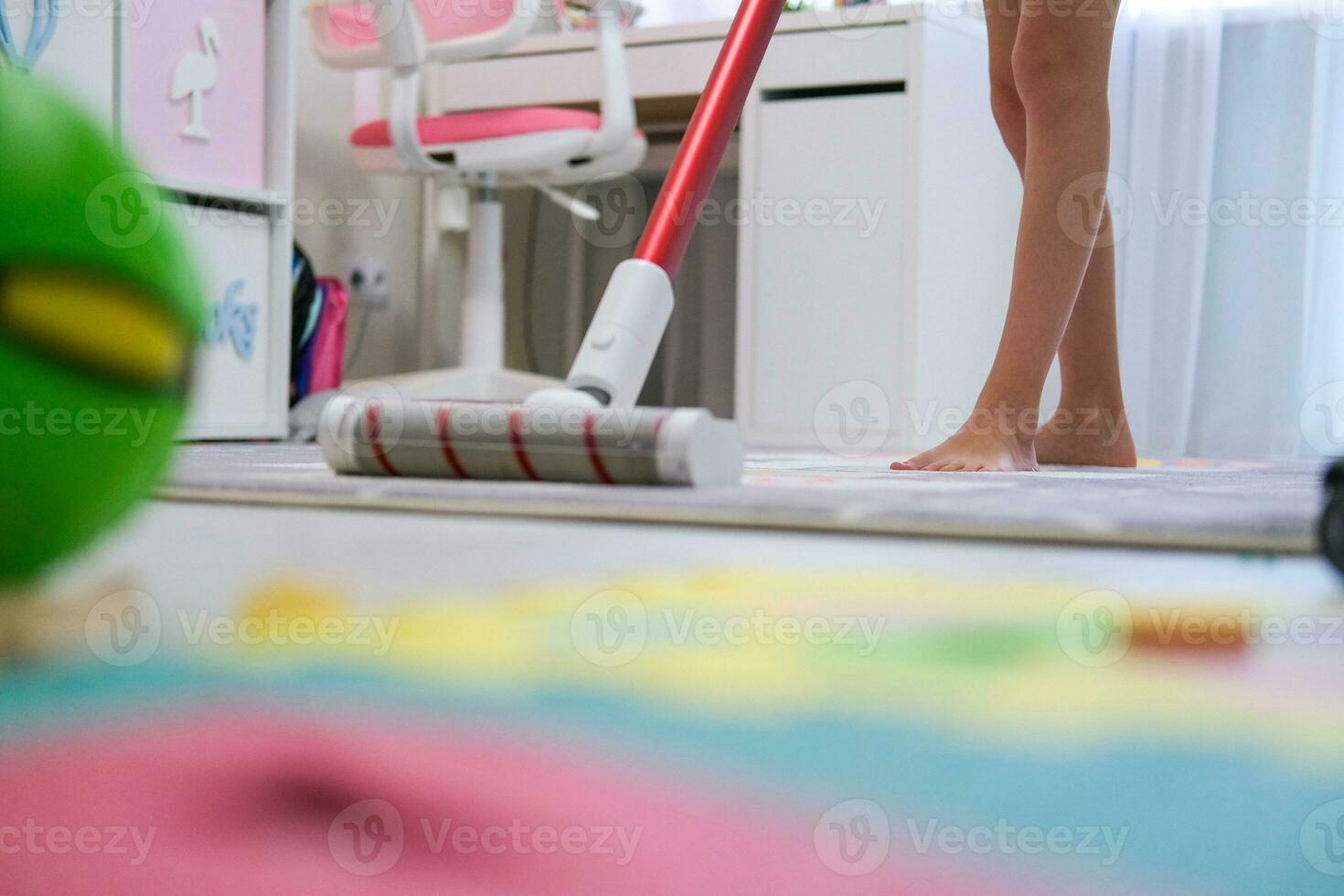 The child vacuums with a cordless vacuum cleaner in the nursery. Cleaning in the children's room, helping parents. photo