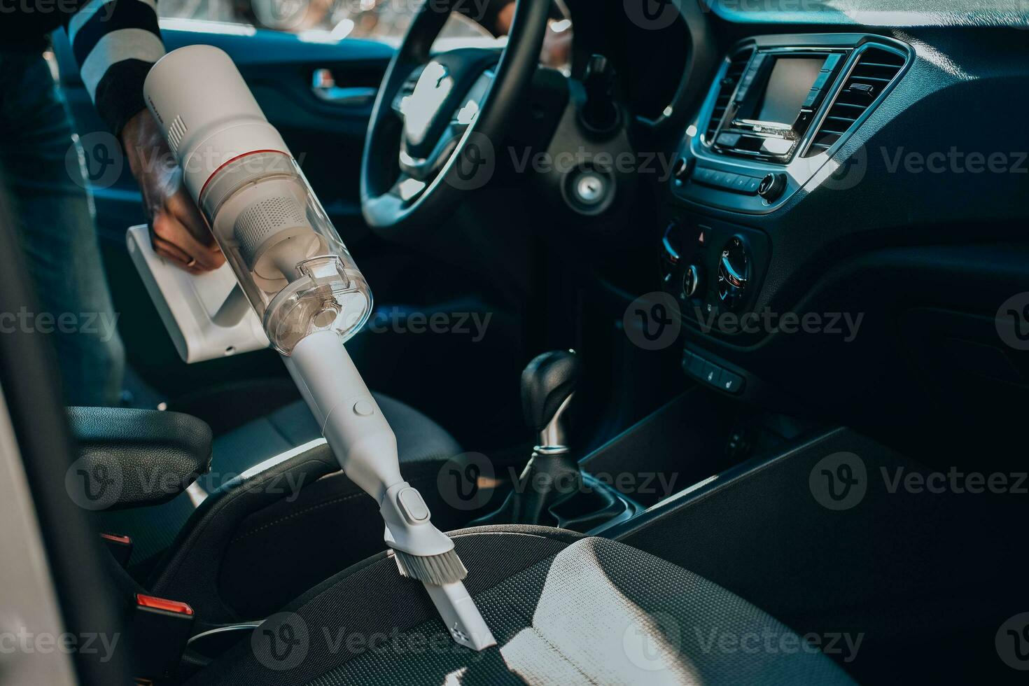 de cerca de un hombre Pasar la aspiradora un coche asiento. el mano sostiene un sin cable vacío limpiador y limpia el interior de el coche. foto