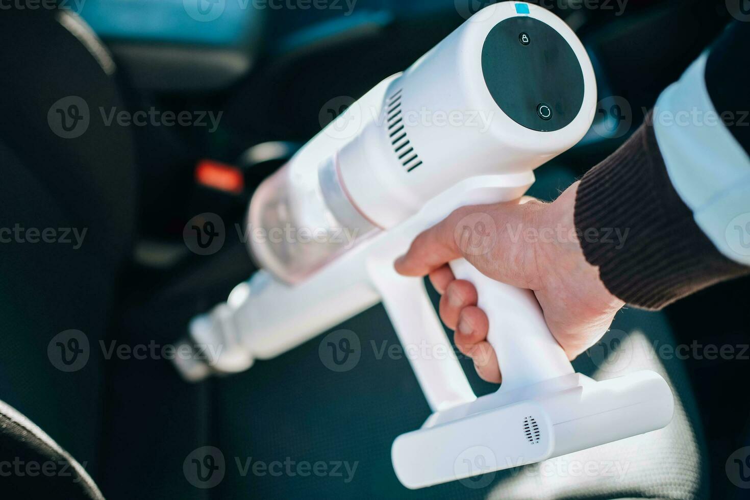 Close-up of a man vacuuming a car seat. The hand holds a cordless vacuum cleaner and cleans the interior of the car. photo