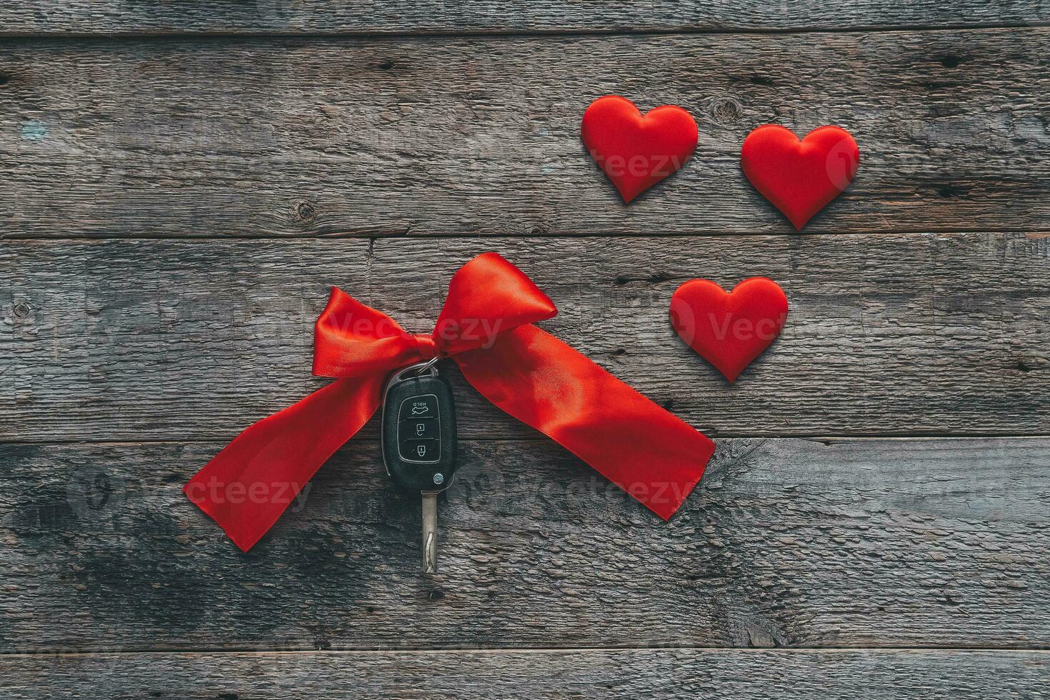 Car keys with red ribbon and heart on wooden background. The concept of a car gift for the holiday of February 14th. Valentine's Day. photo