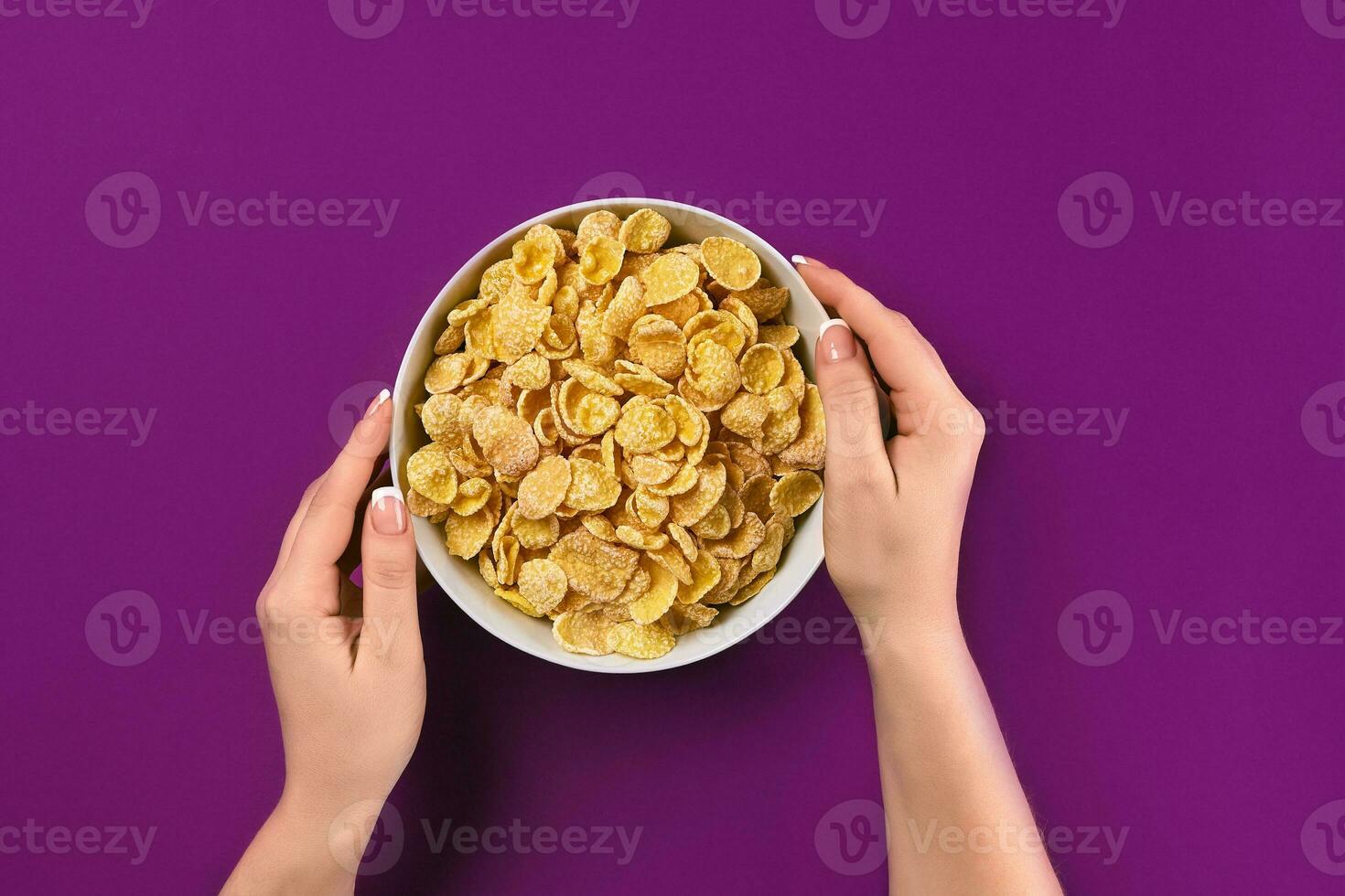 Female hands holding bowl with healthy breakfast, closeup. Bowl with cornflakes on the colorful background photo