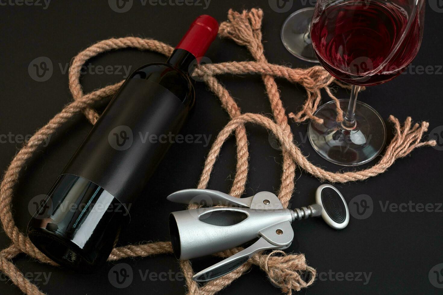 Red wine bottle, two glasses and corkscrew on black background. Top view photo