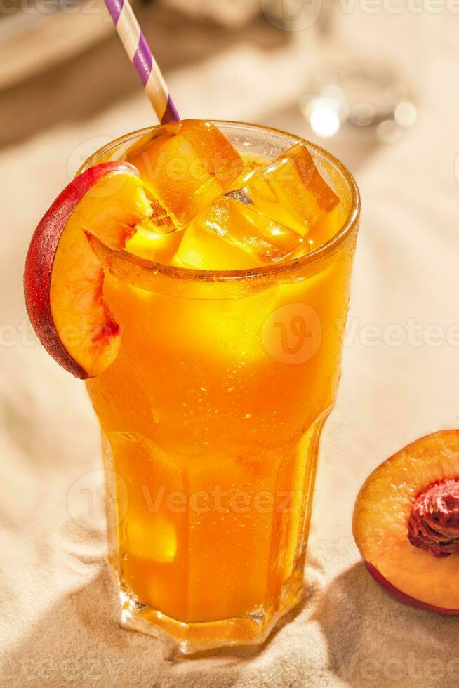 Summer cold drinks peach sangria with ice cubes in glass on sand background photo