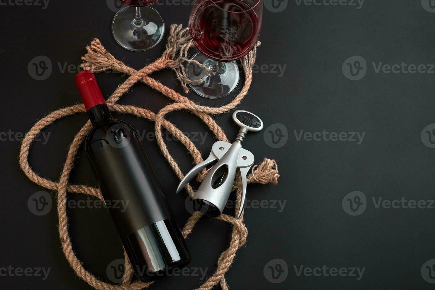 Red wine bottle, two glasses and corkscrew on black background. Top view with copy space photo