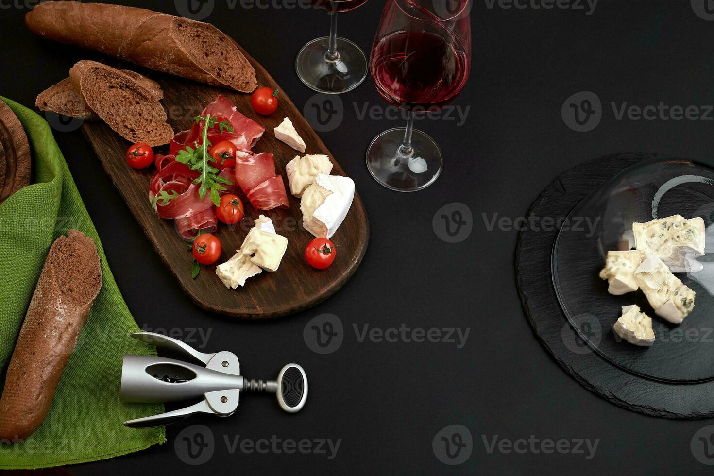 jamón, salami, junquillo rebanadas, Tomates y nutson rústico de madera junta, dos lentes de rojo vino terminado negro antecedentes foto