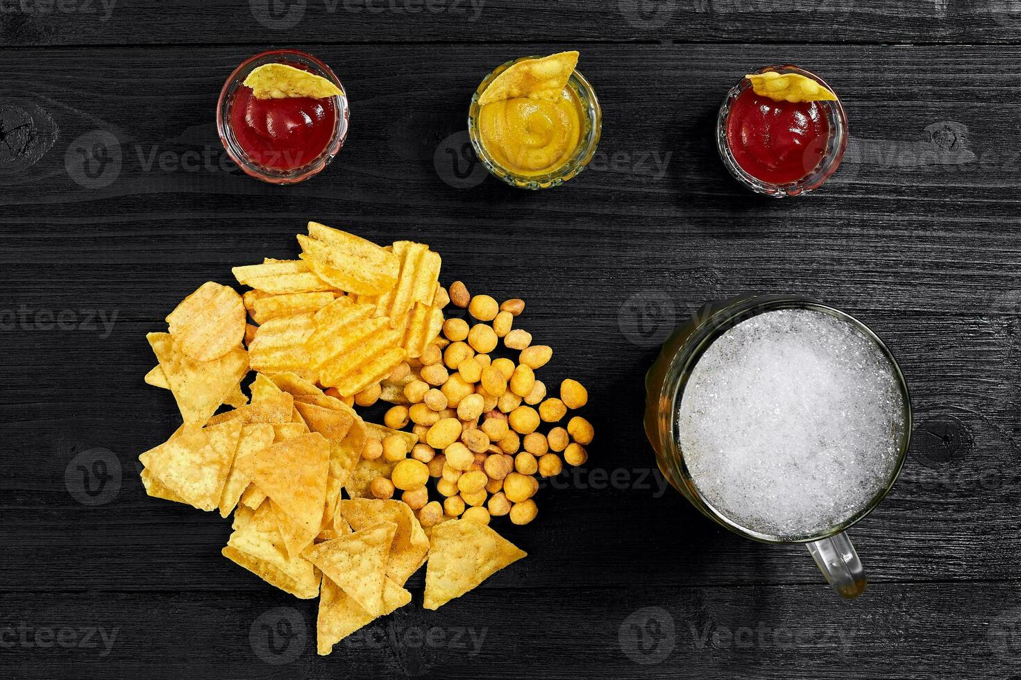 Overhead view of beer glass and snacks with sauce on black wooden table. photo