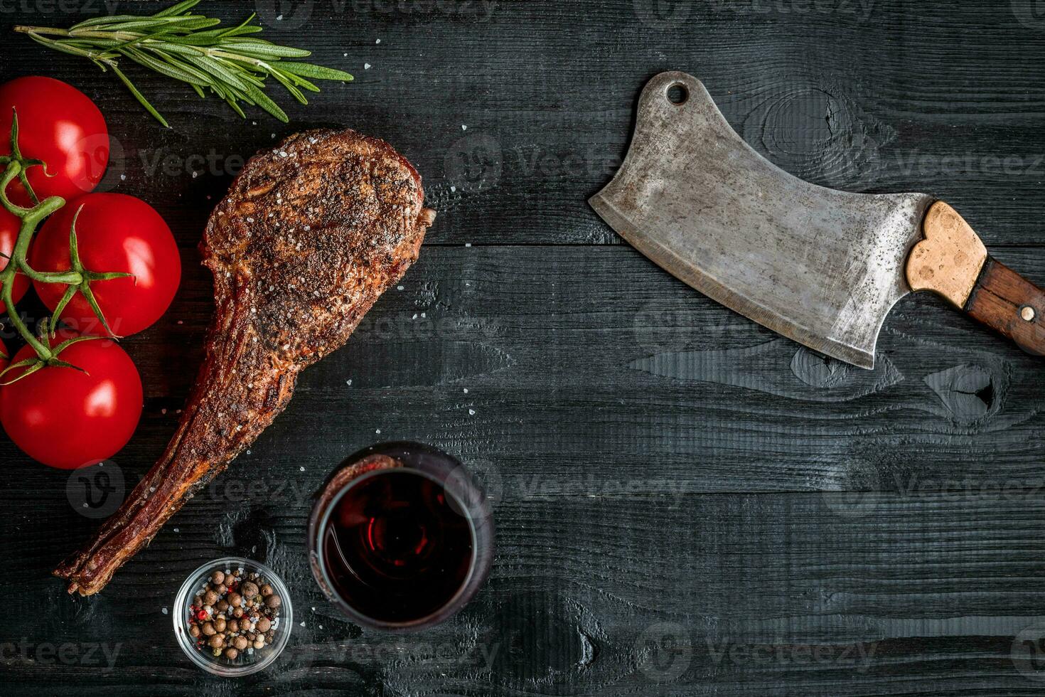 Barbecue dry aged rib of beef with spice, vegetables and glass of red wine close-up on black wooden background photo