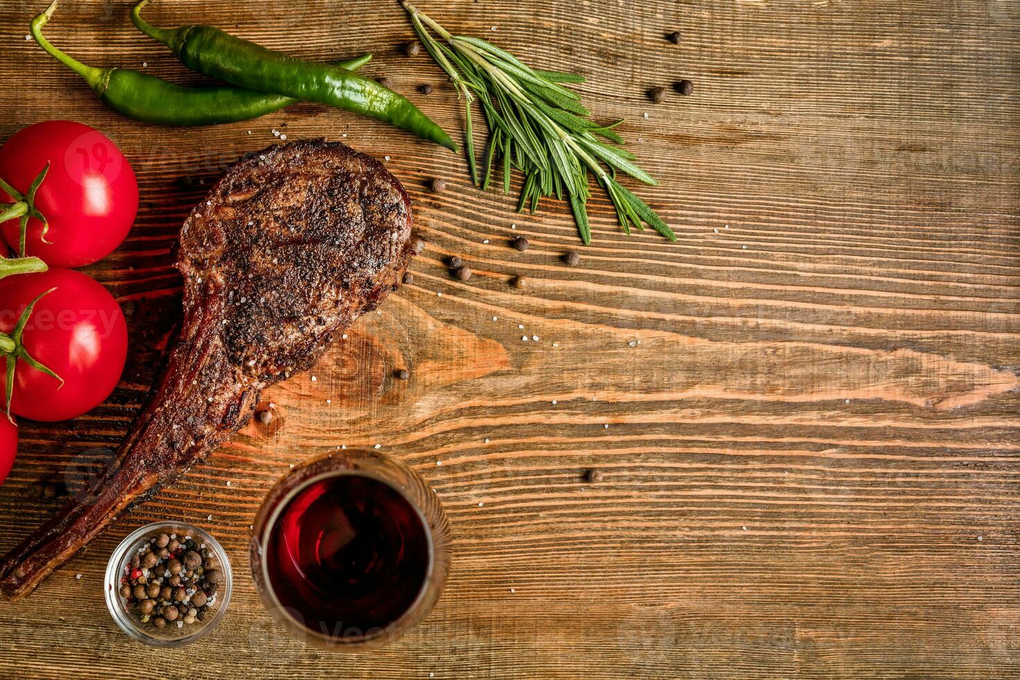 Barbecue dry aged rib of beef with vegetables and glass of red wine close-up on wooden background photo