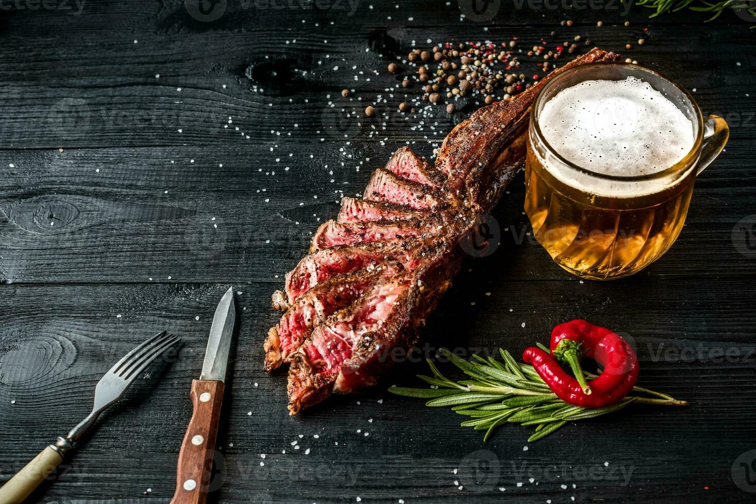 Barbecue dry aged rib of beef with spice, vegetables and a glass of light beer close-up on black wooden background photo