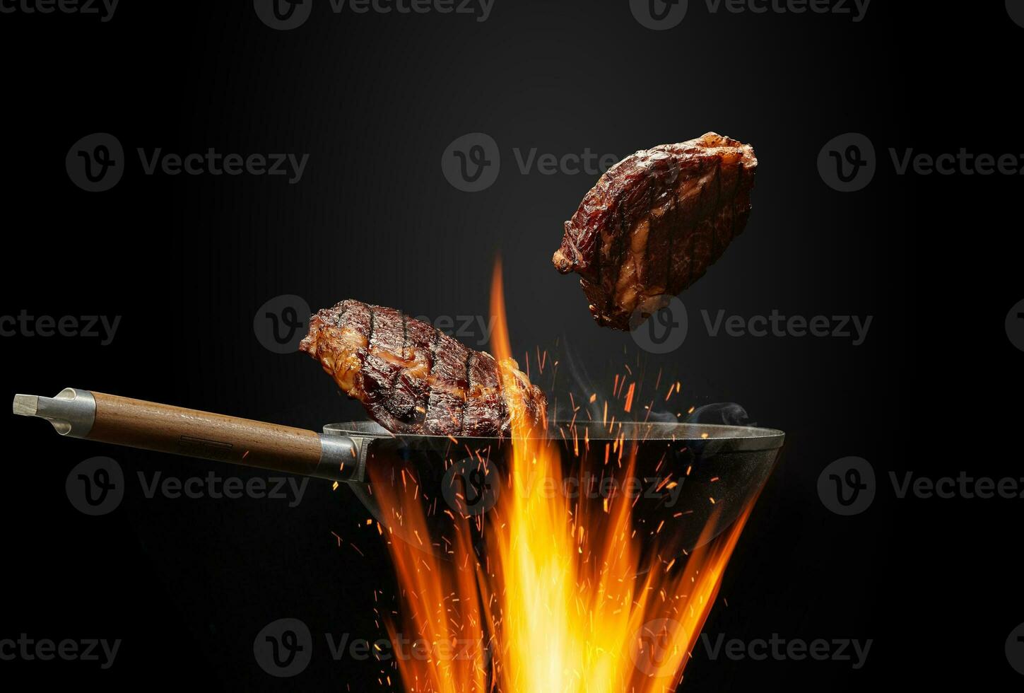 Wok pan with smoke above fire is frying two beef steaks against black studio background. Cooking concept. Close up photo