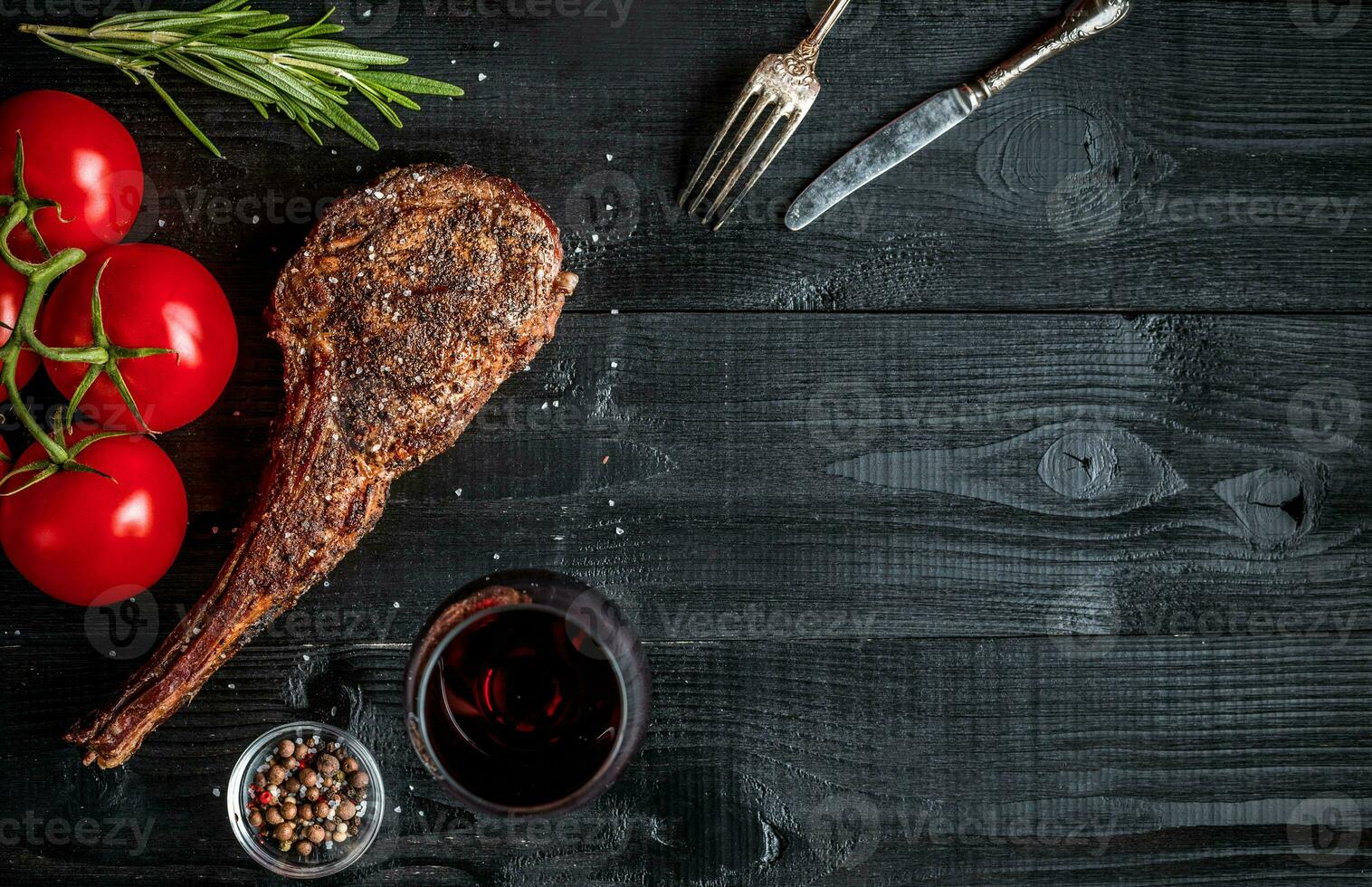 Barbecue dry aged rib of beef with spice, vegetables and glass of red wine close-up on black wooden background photo