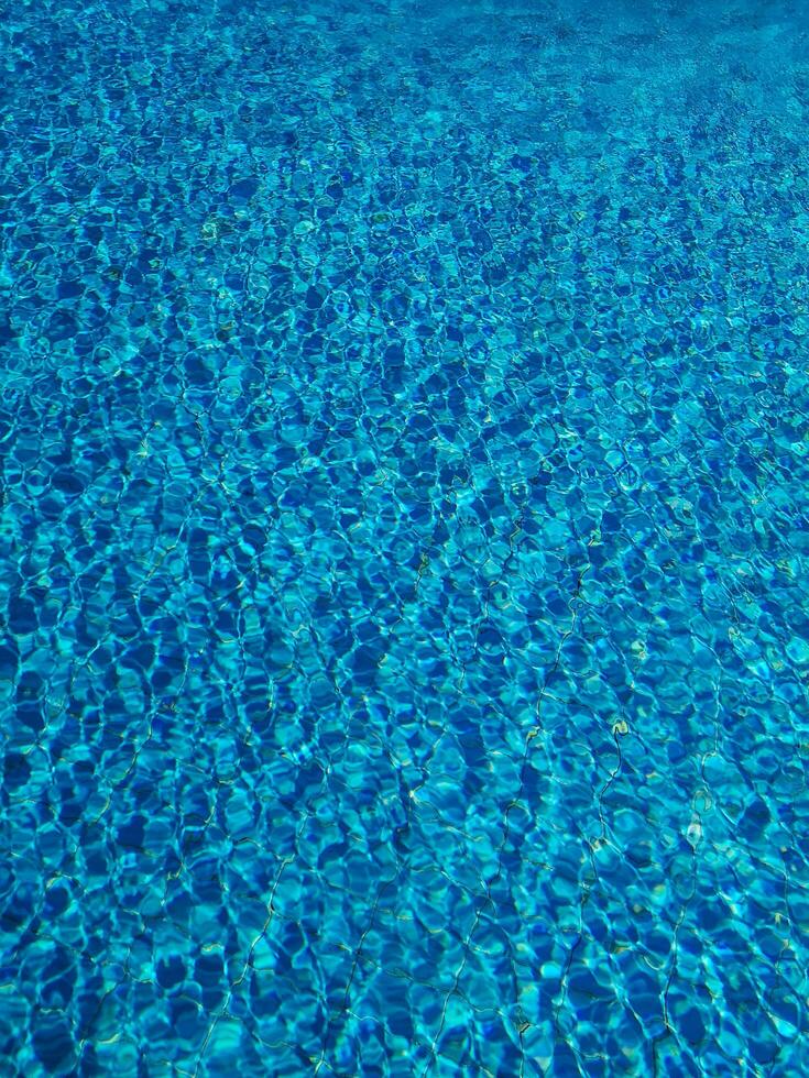 Blue water ripple in swimming pool with sun reflections photo