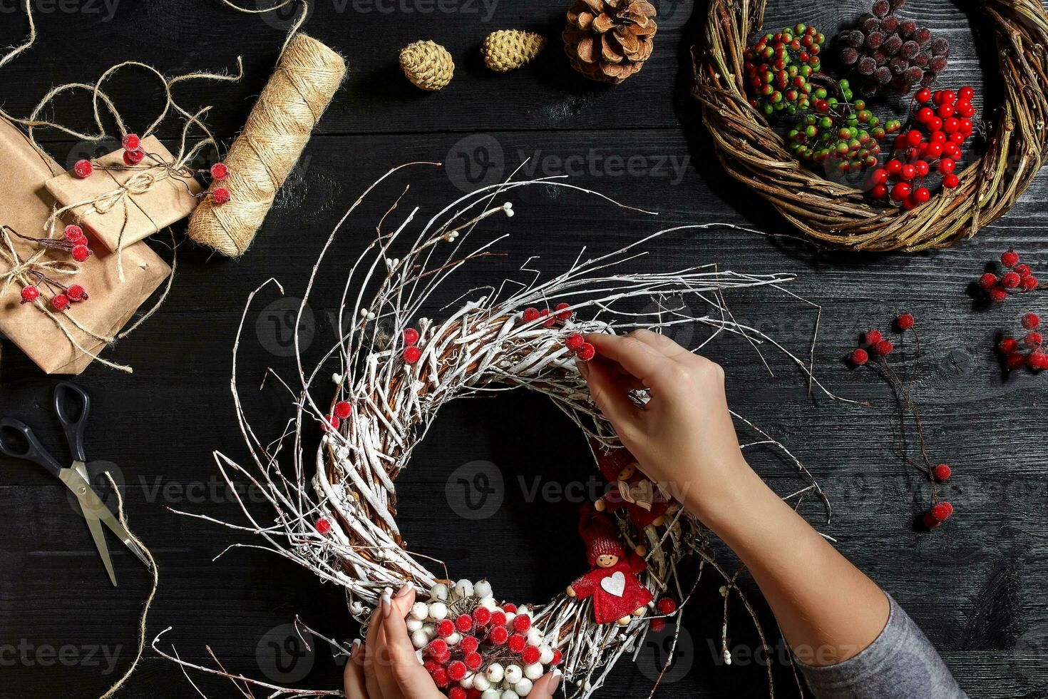 Top view of female hands make a Christmas wreath. Packed gifts and scrolls, spruce branches and tools on wooden table. photo
