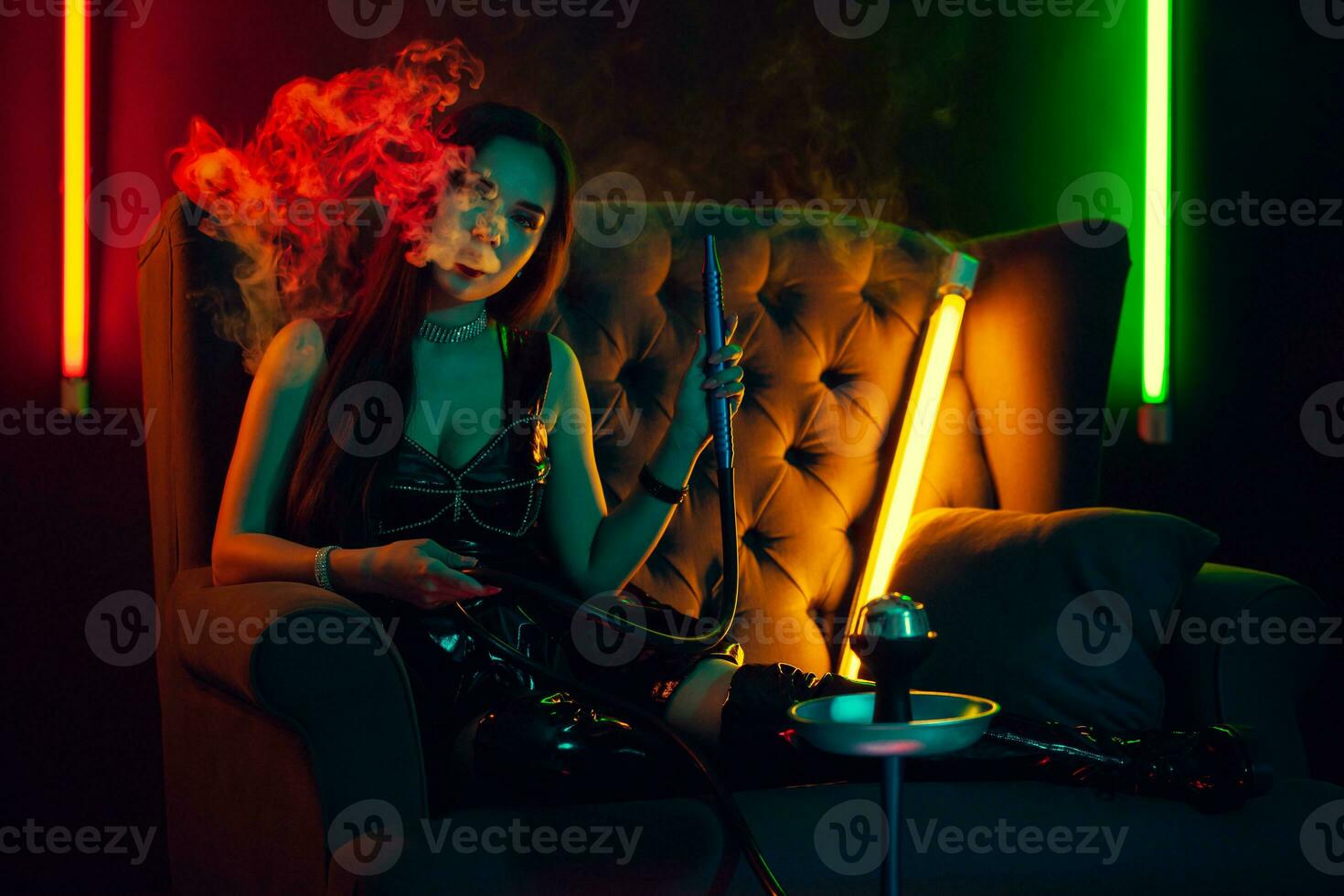sexy morena modelo es de fumar un narguile exhalando un fumar a un lujo noche club. foto