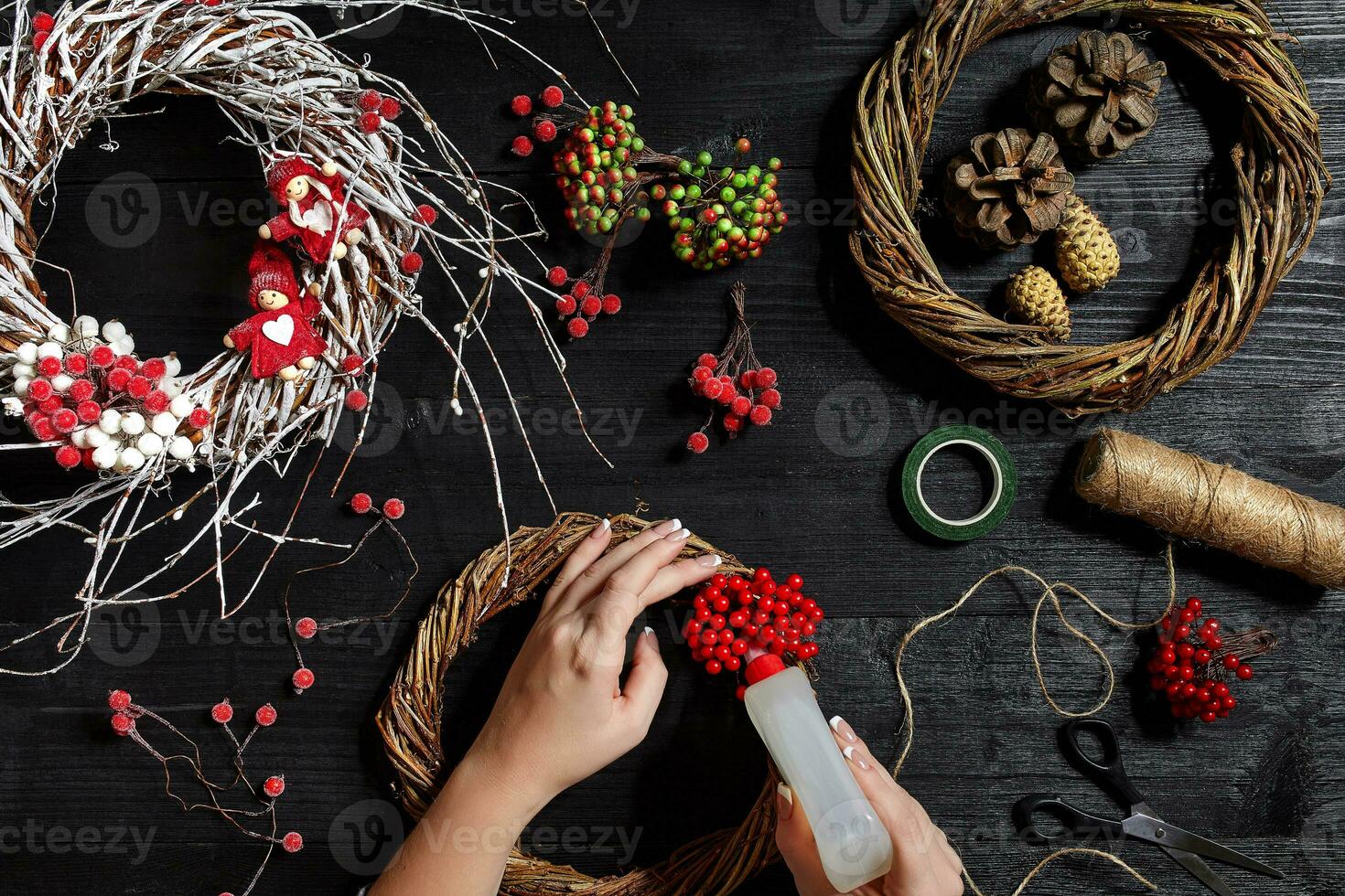 Top view of female hands make a Christmas wreath. Packed gifts and scrolls, spruce branches and tools on wooden table. photo