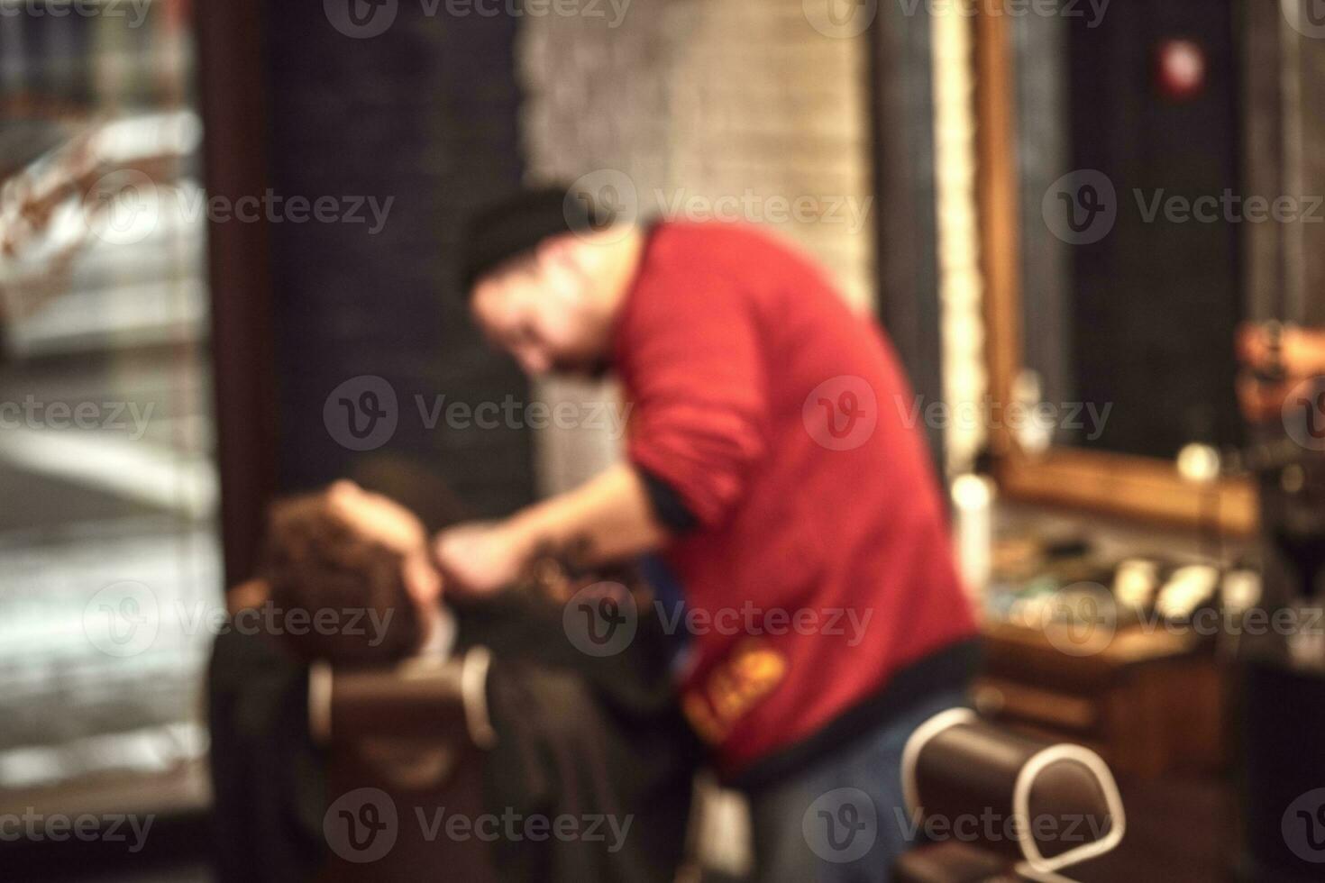 A strong handsome man getting shaved by a professional barber in a barbershop. Blurred image. photo