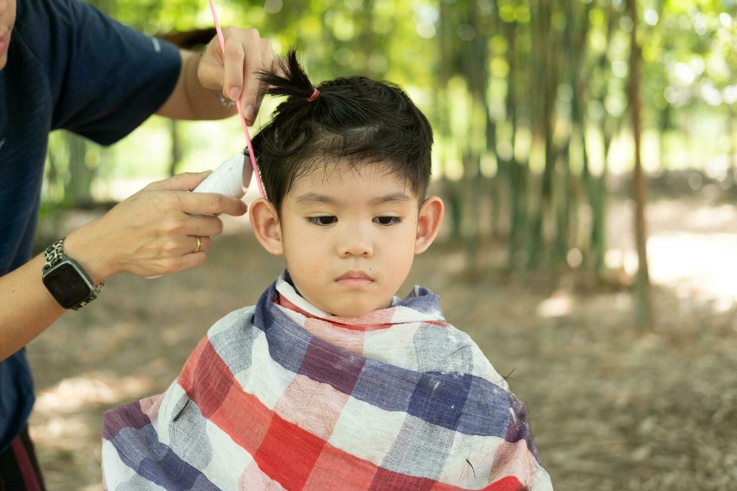 Barbero corte pelo de un asiático chico en un abierto espacio lleno con arboles foto