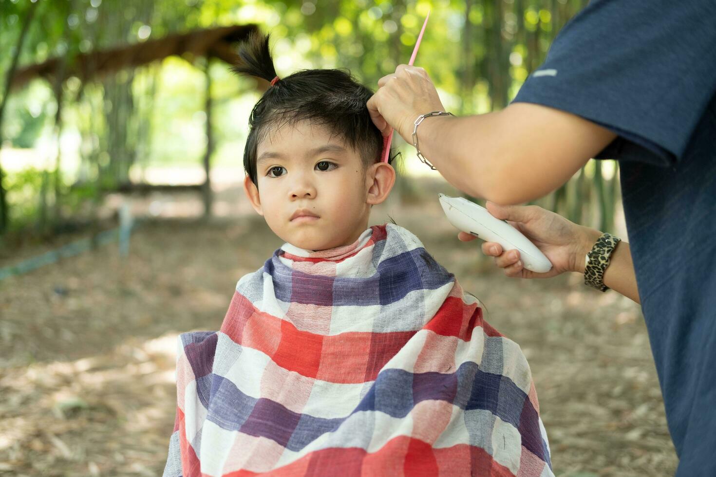 Barbero corte pelo de un asiático chico en un abierto espacio lleno con arboles foto
