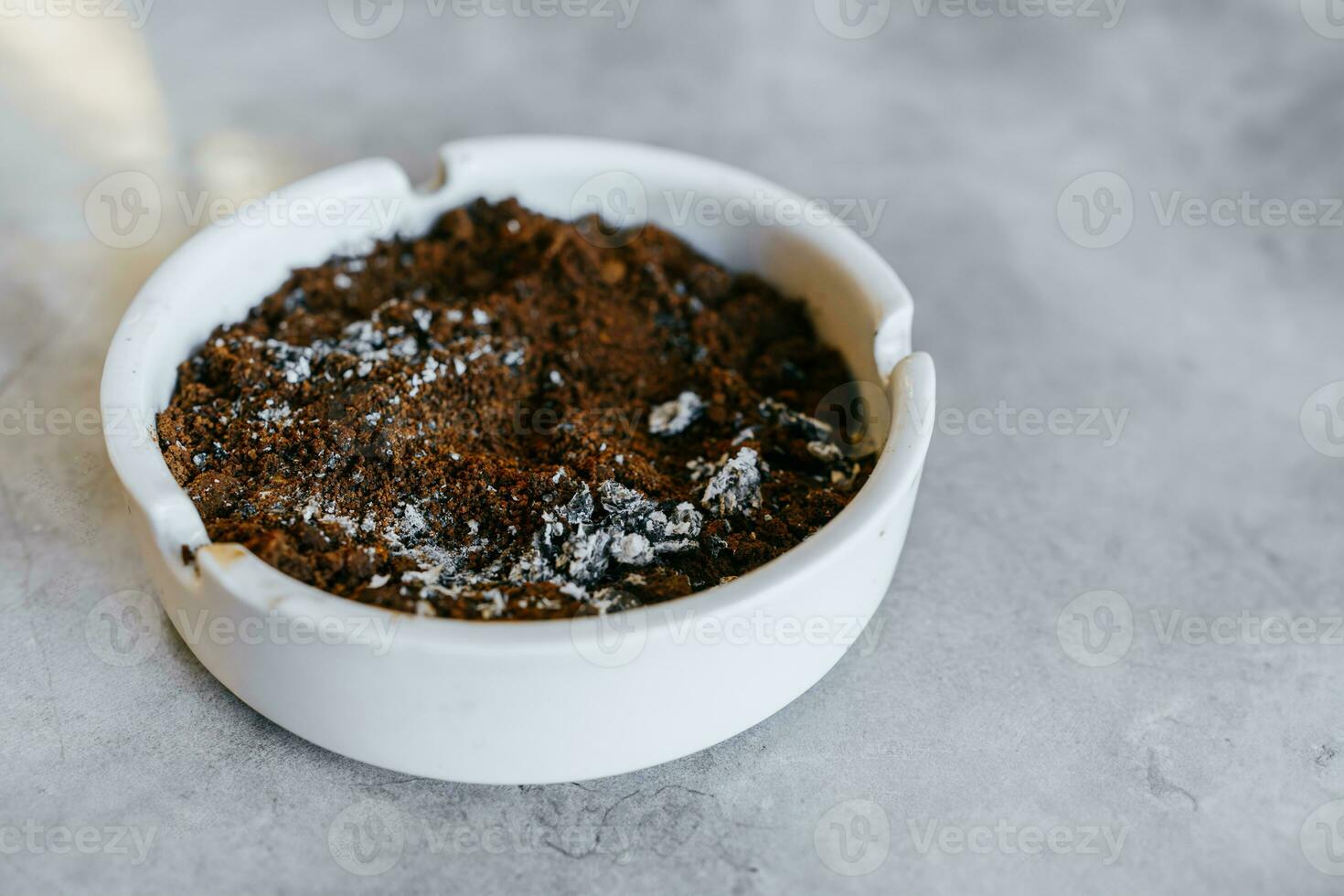 Dried coffee grounds and cigarette ash in a white ashtray. Copy space. White ashtray on gray ceramic table. photo