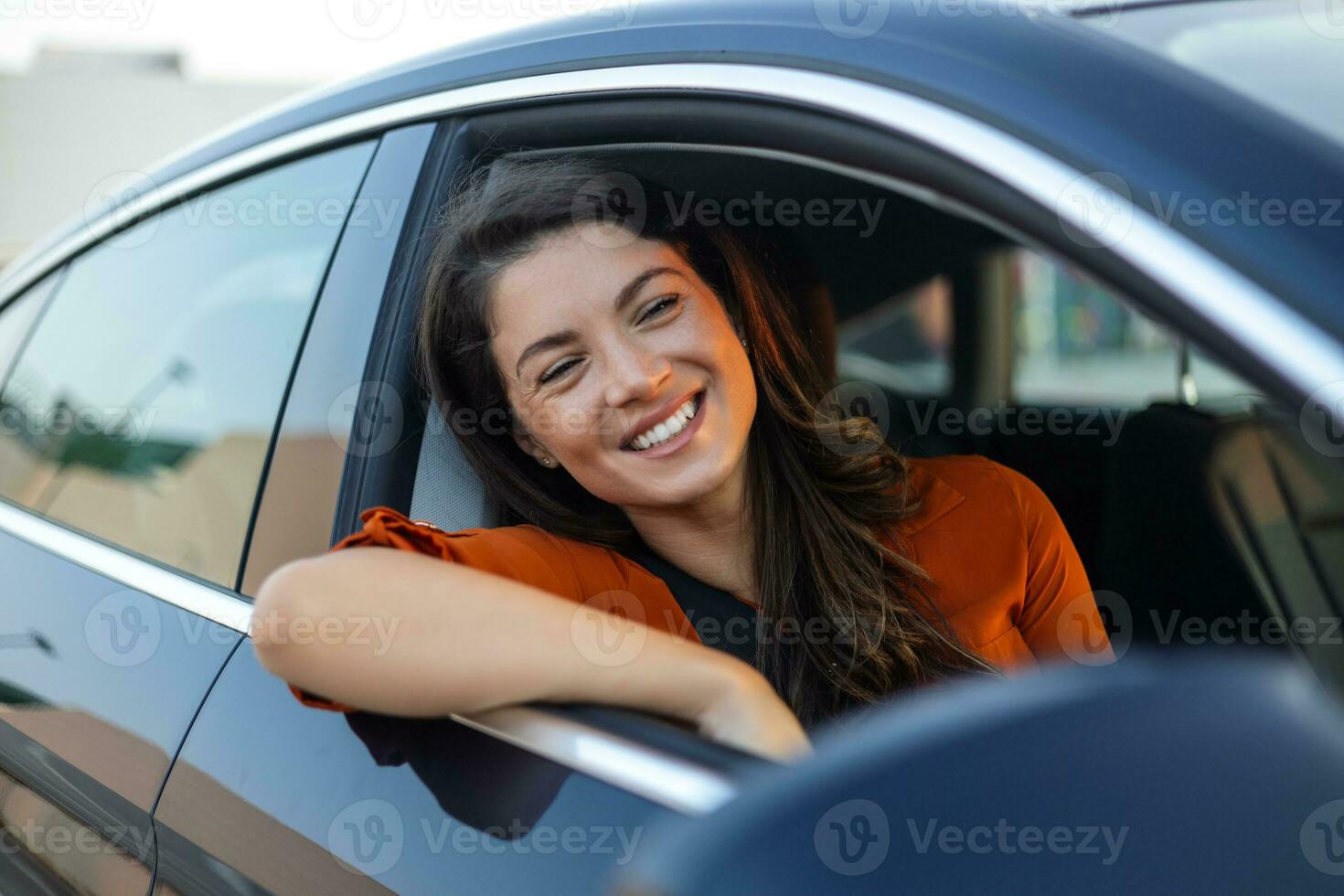 Young woman sitting in a car hand out of window. Happy woman driving a car and smiling. Portrait of happy female driver steering car with safety belt. Cute young lady happy driving car. photo