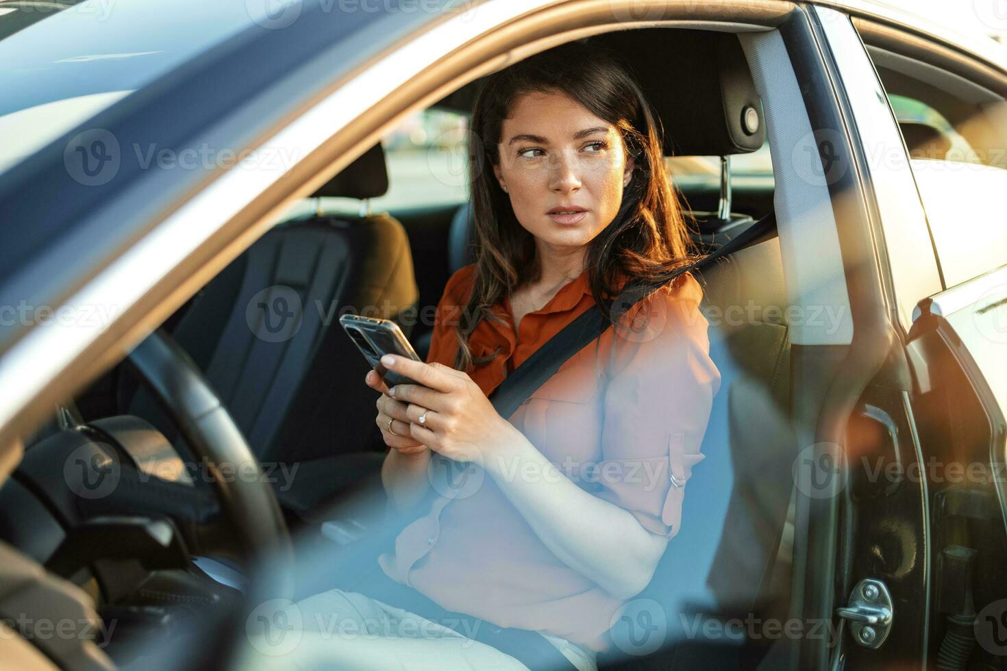 Portrait of a young woman texting on her smartphone while driving a car. Business woman sitting in car and using her smartphone. female driver and phone screen photo