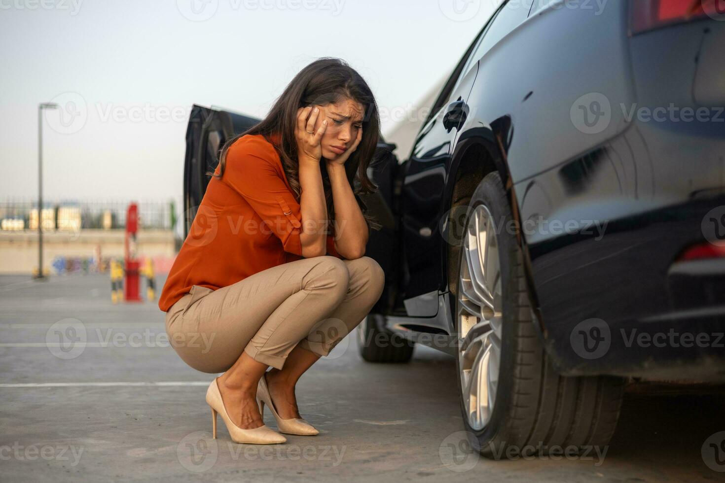 Portrait of a despair woman crouching next to her car with flat tire, problems on the road, deflated tire. photo
