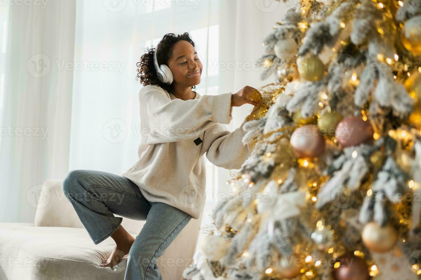 Merry Christmas. African American woman wearing headphones listening music decorating Christmas tree. Happy girl near classical traditional Christmas tree. Christmas eve at home time for celebration. photo