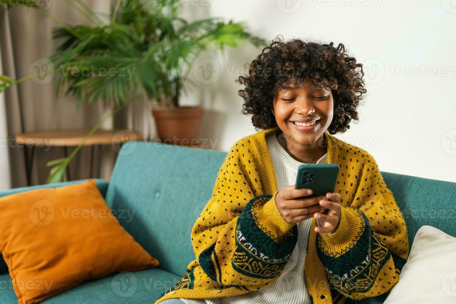 African girl holding smartphone touch screen typing scroll page at home. Woman with cell phone surfing internet using social media apps playing game. Shopping online Internet news cellphone addiction. photo