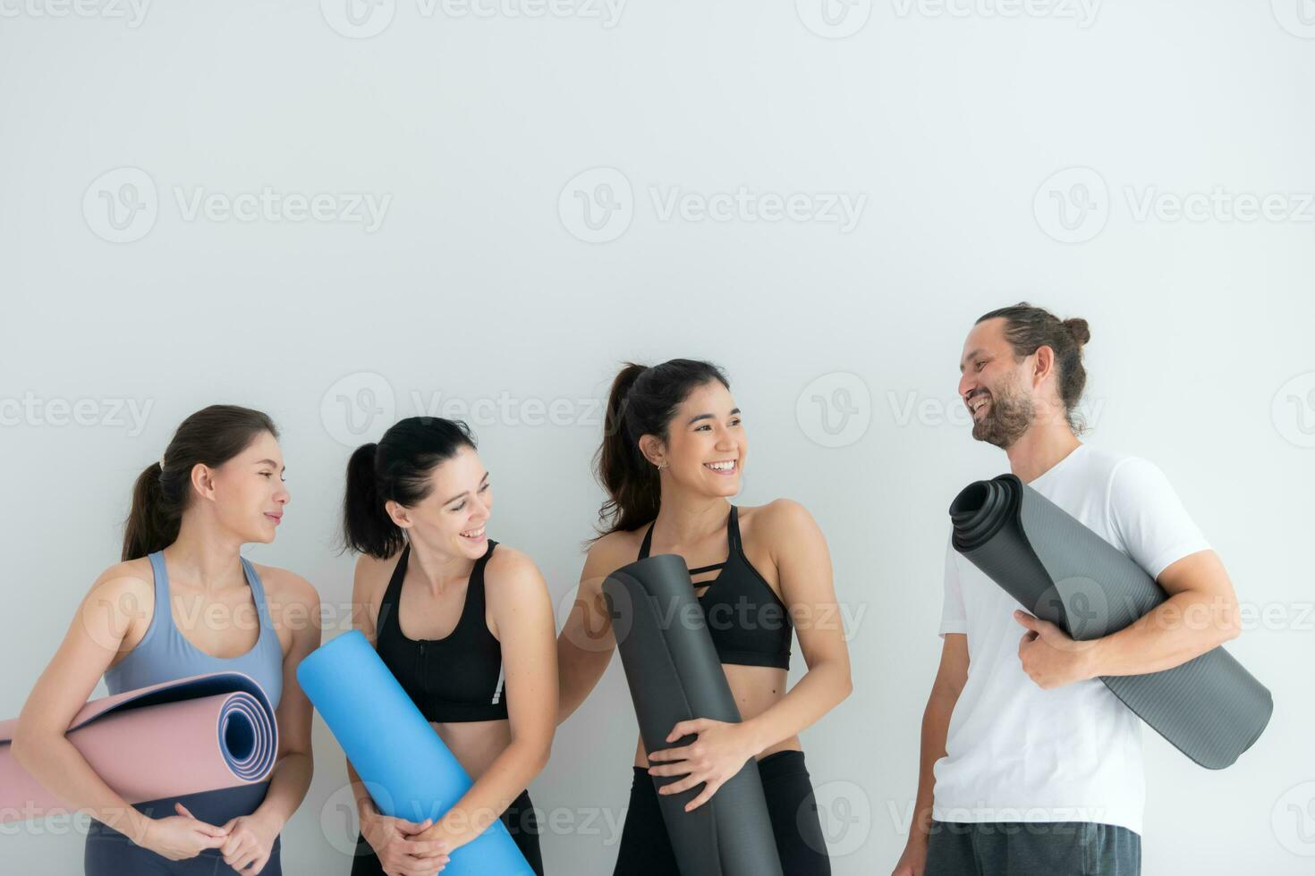 un grupo de hembra y masculino Atletas destacado y charlamos amistosamente en el estudio antes de comenzando con el yoga clase. foto