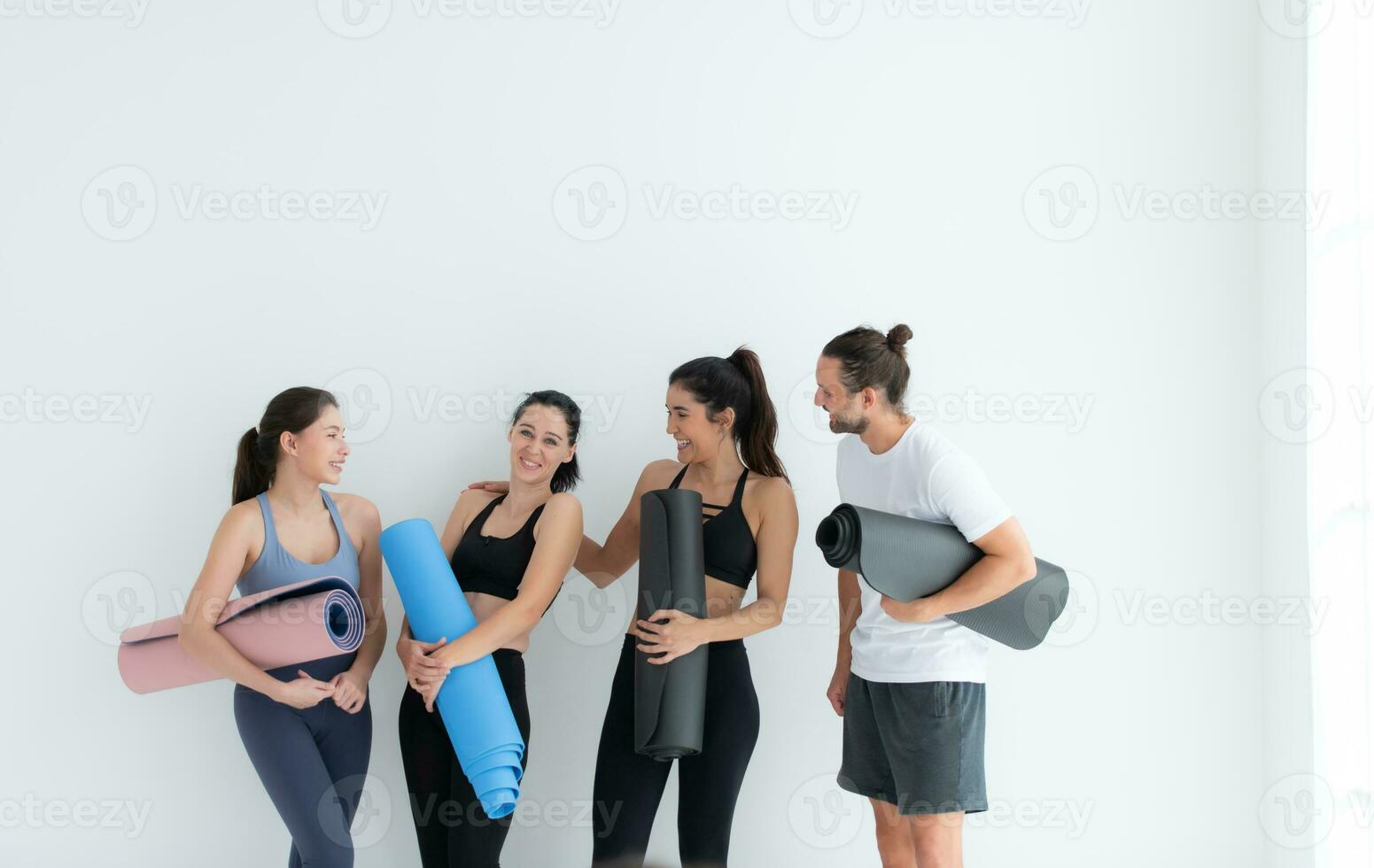 A group of female and male athletes stood and chatted amicably in the studio before beginning with the yoga class. photo