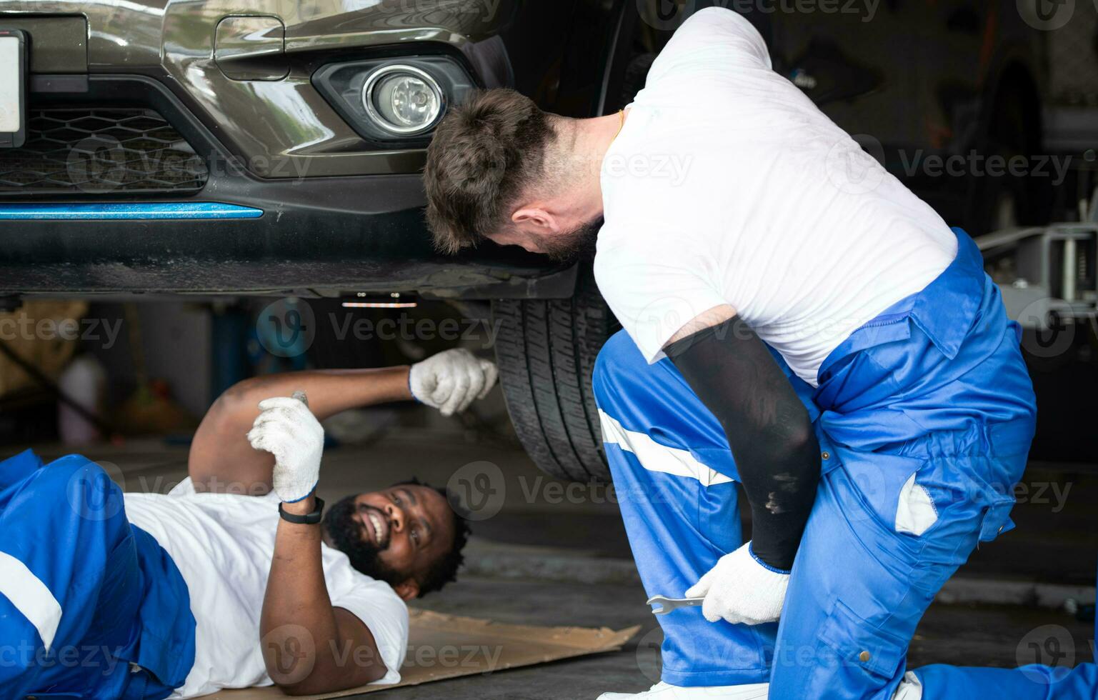 ambos de coche mecánico trabajando en un auto reparar comercio, cheque el operación de el motor de debajo el coche ese viene en para refacción a el auto reparar tienda. foto