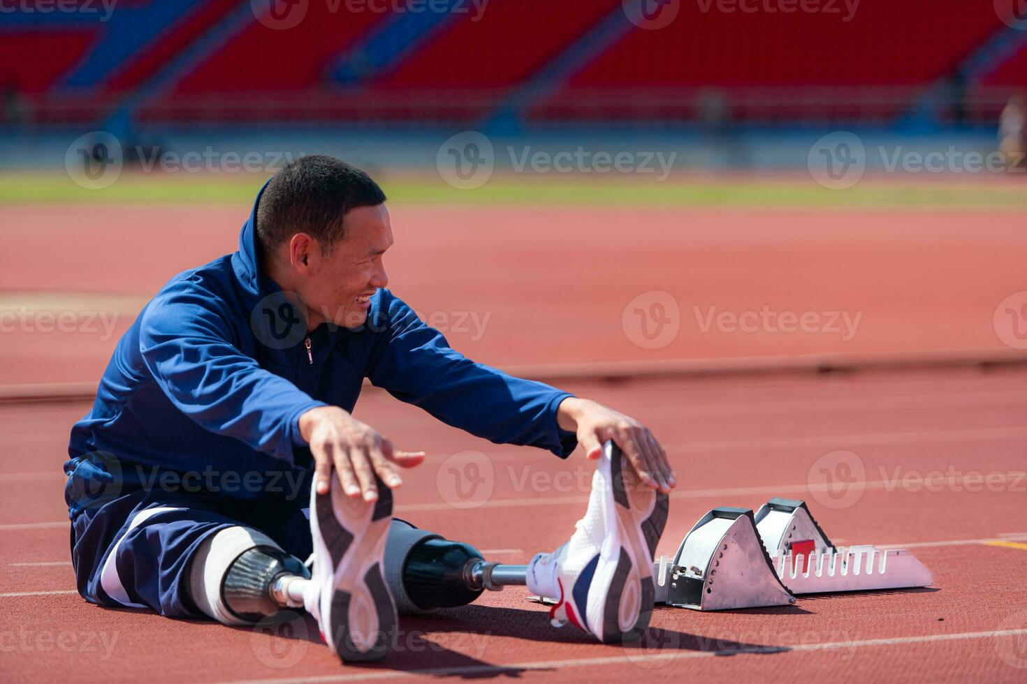 Disabled athletic man stretching and warming up before running on stadium track photo