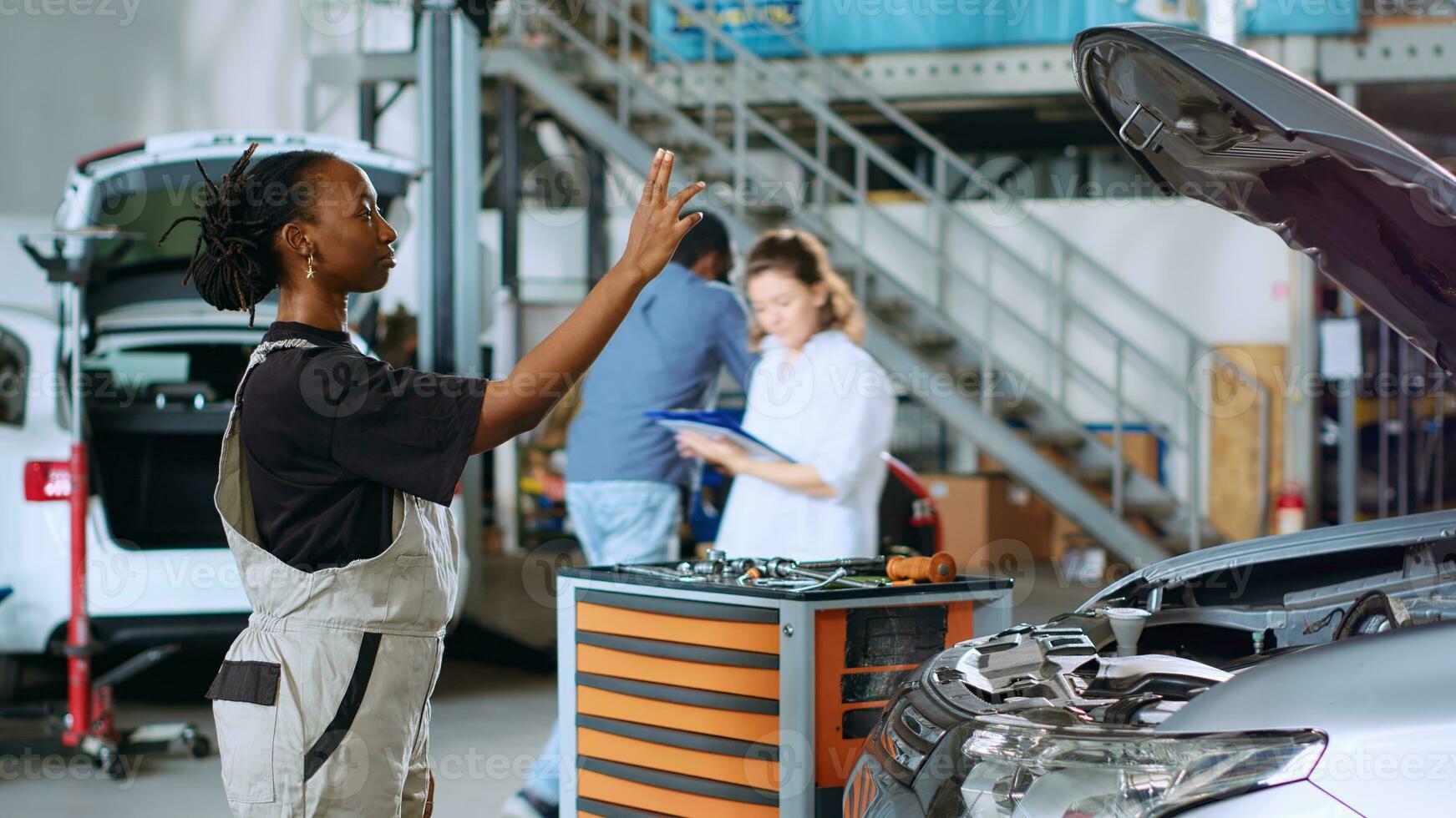 con licencia ingeniero en auto reparar tienda utilizando aumentado realidad holograma a visualizar coche componentes en orden a reparar a ellos. africano americano mujer utilizando Arkansas tecnología mientras trabajando en dañado vehículo foto