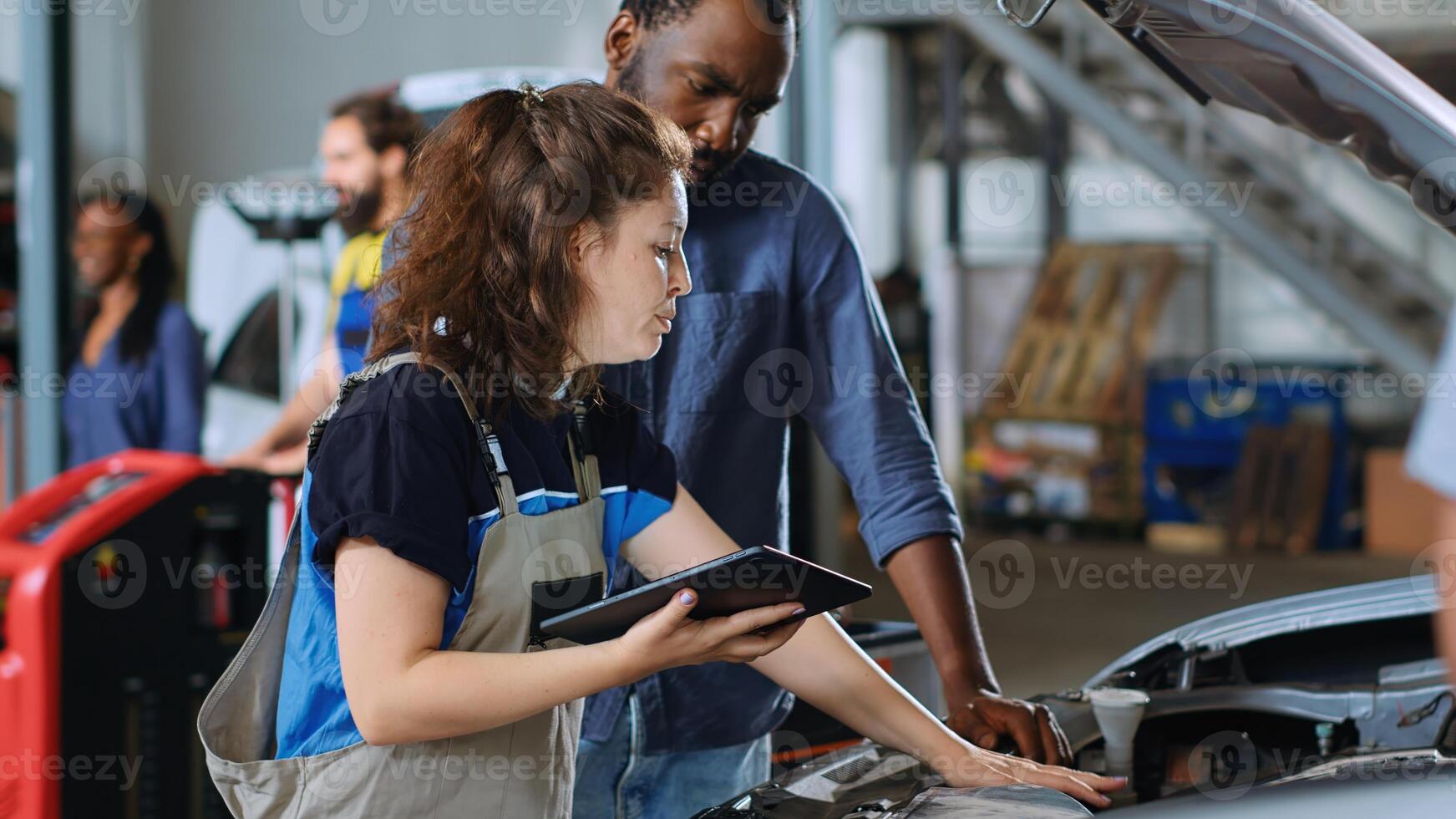 Mechanic in car service uses tablet to calculate invoice after fixing broken automobile engine. Auto repair shop worker uses device to inform man of final costs after repairing vehicle, close up photo